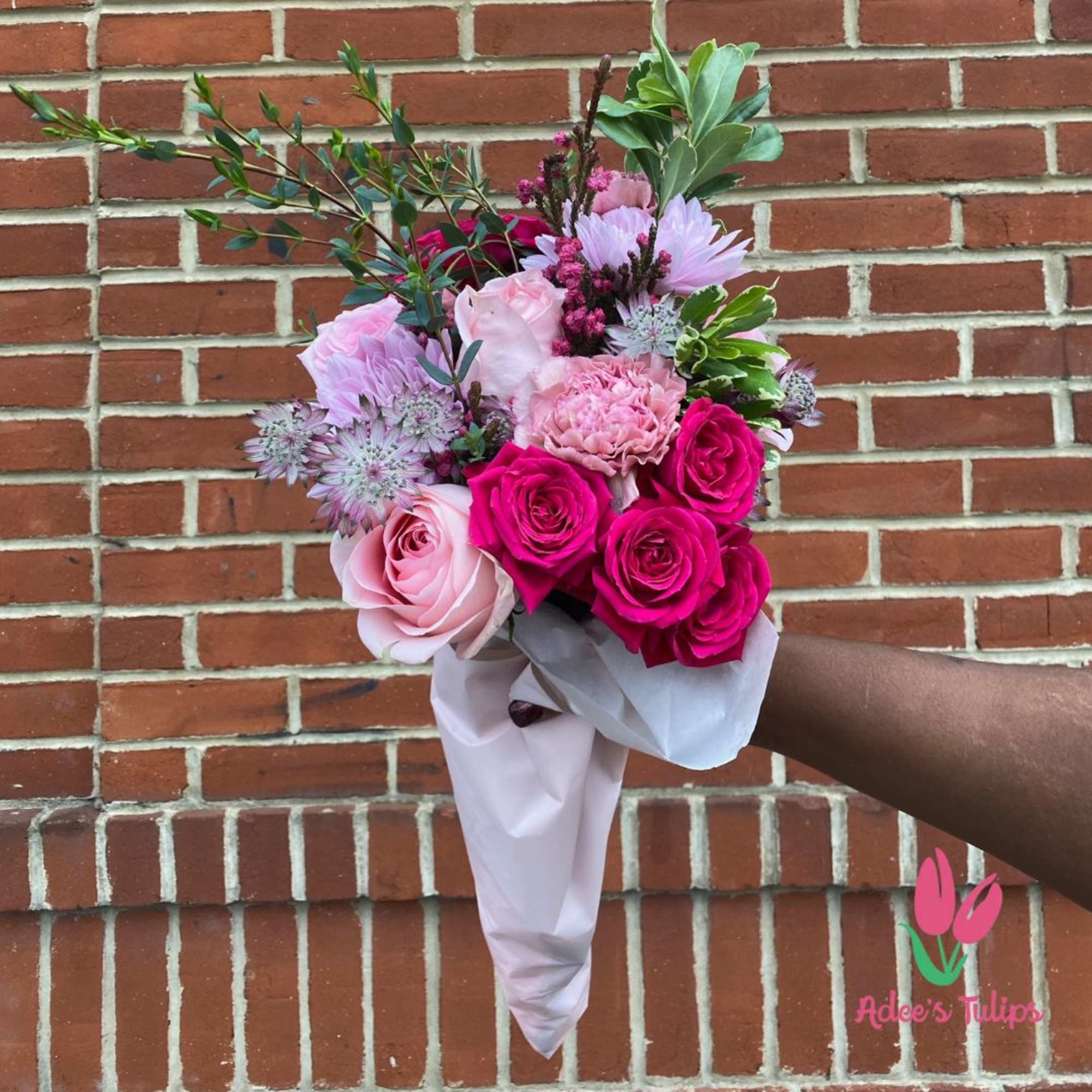 Handheld bouquet of pink roses and mixed blooms wrapped in pale paper