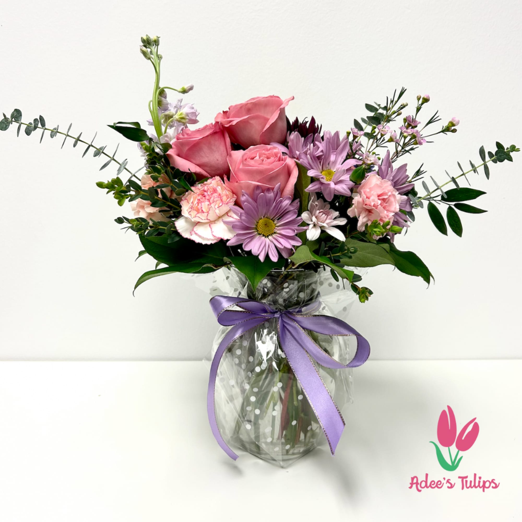 Pink roses and lavender daisies in a glass vase with a purple ribbon