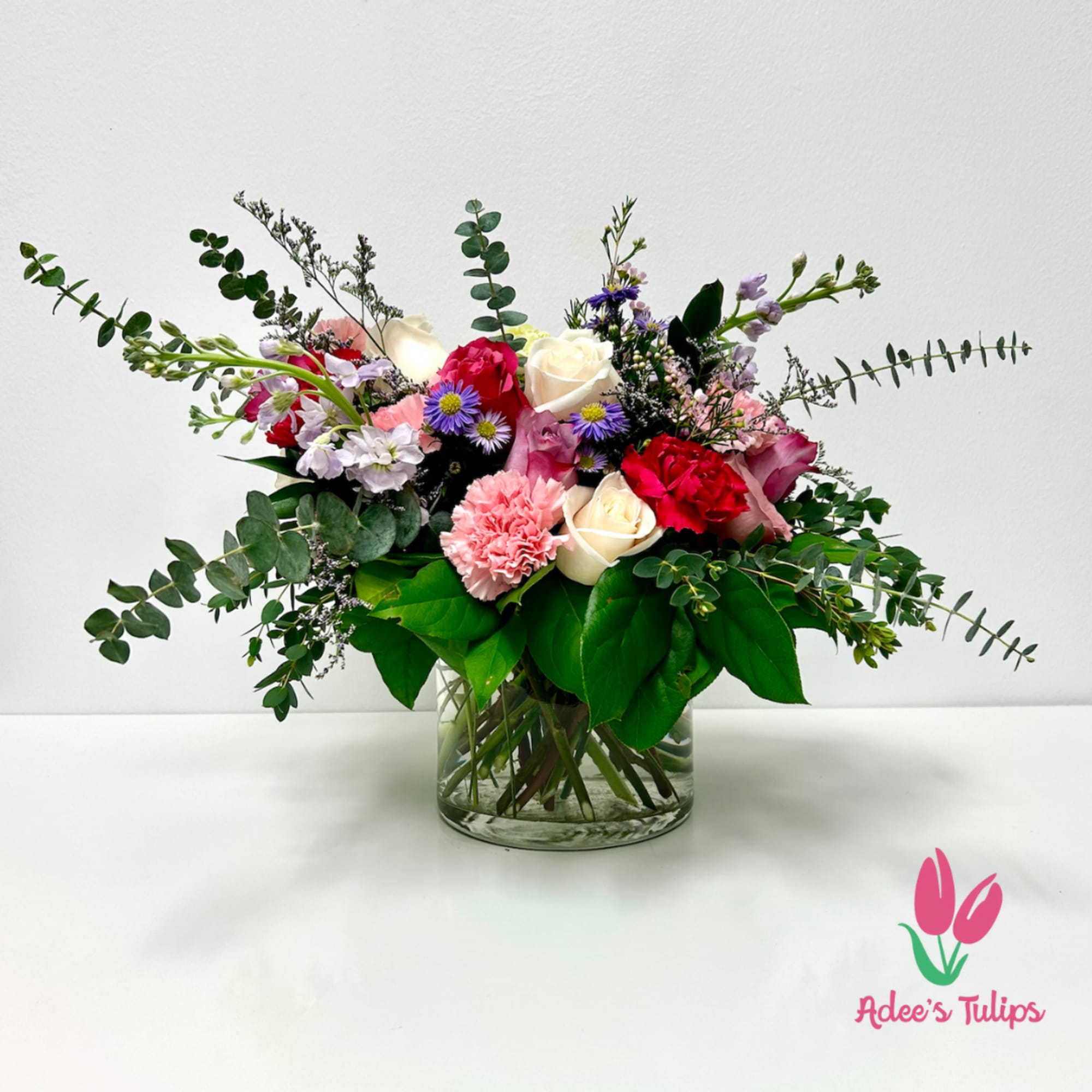 Mixed bouquet of roses, carnations, and purple daisies in a glass vase