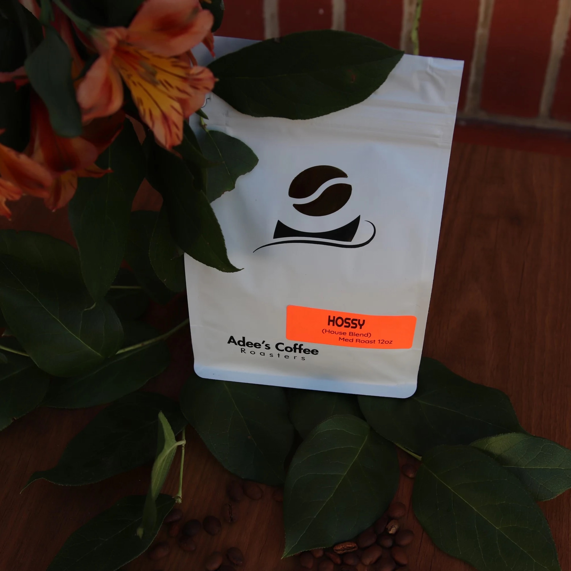 Orange flowers beside a white coffee bag on a wooden surface