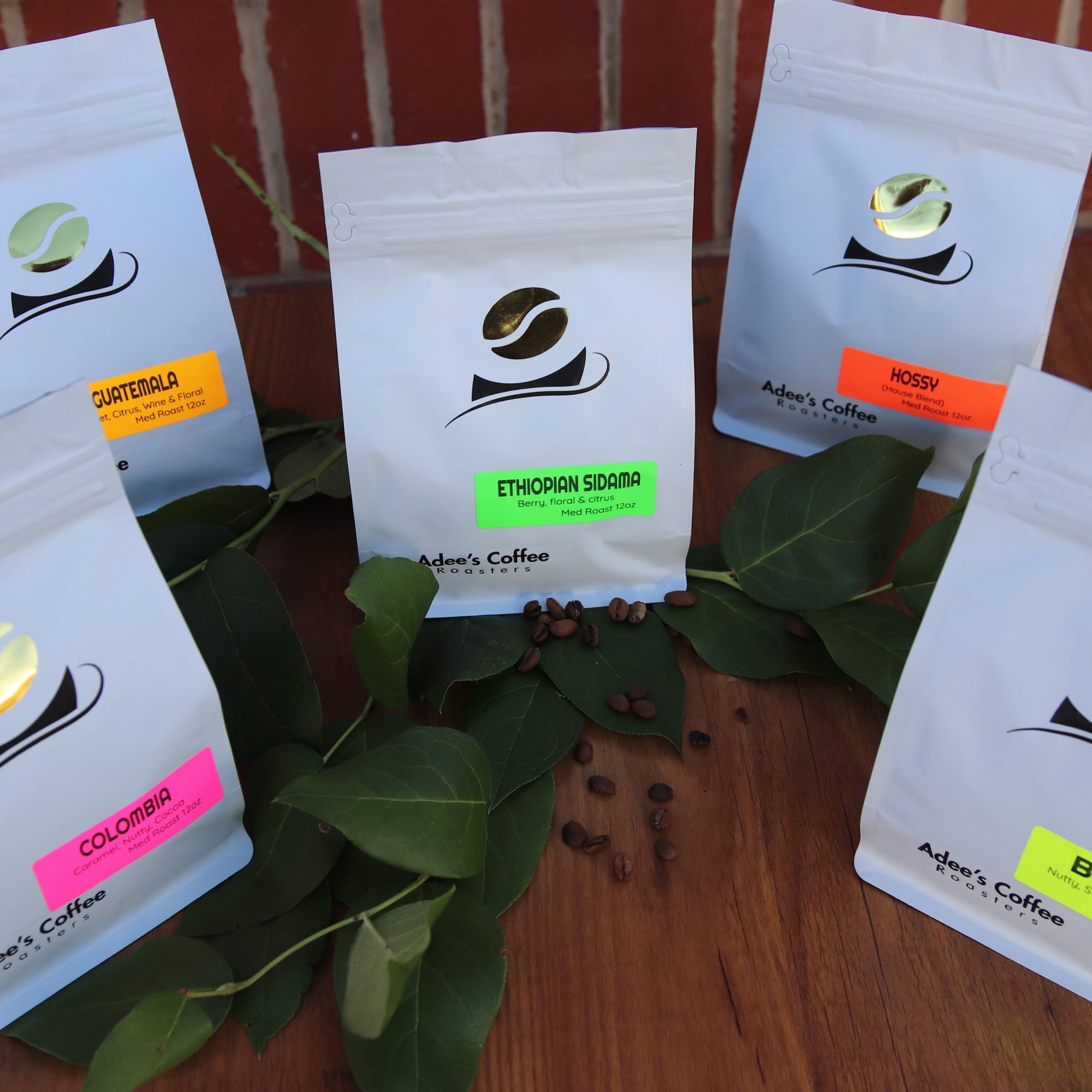 Five coffee bags arranged on a wooden surface with scattered beans and leaves.