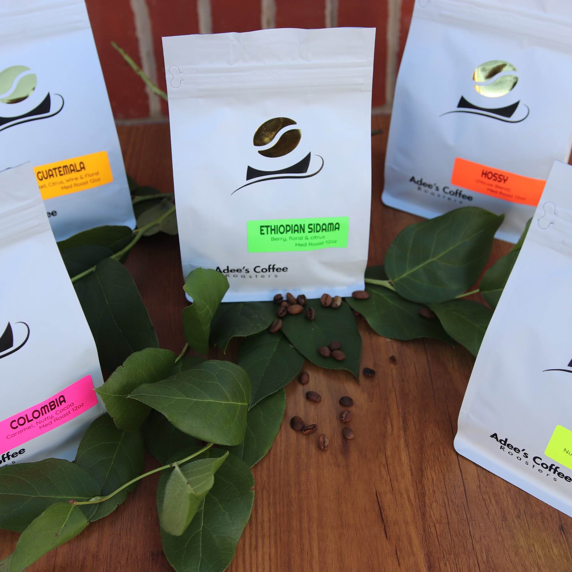 Five coffee bags arranged with scattered coffee beans and green leaves
