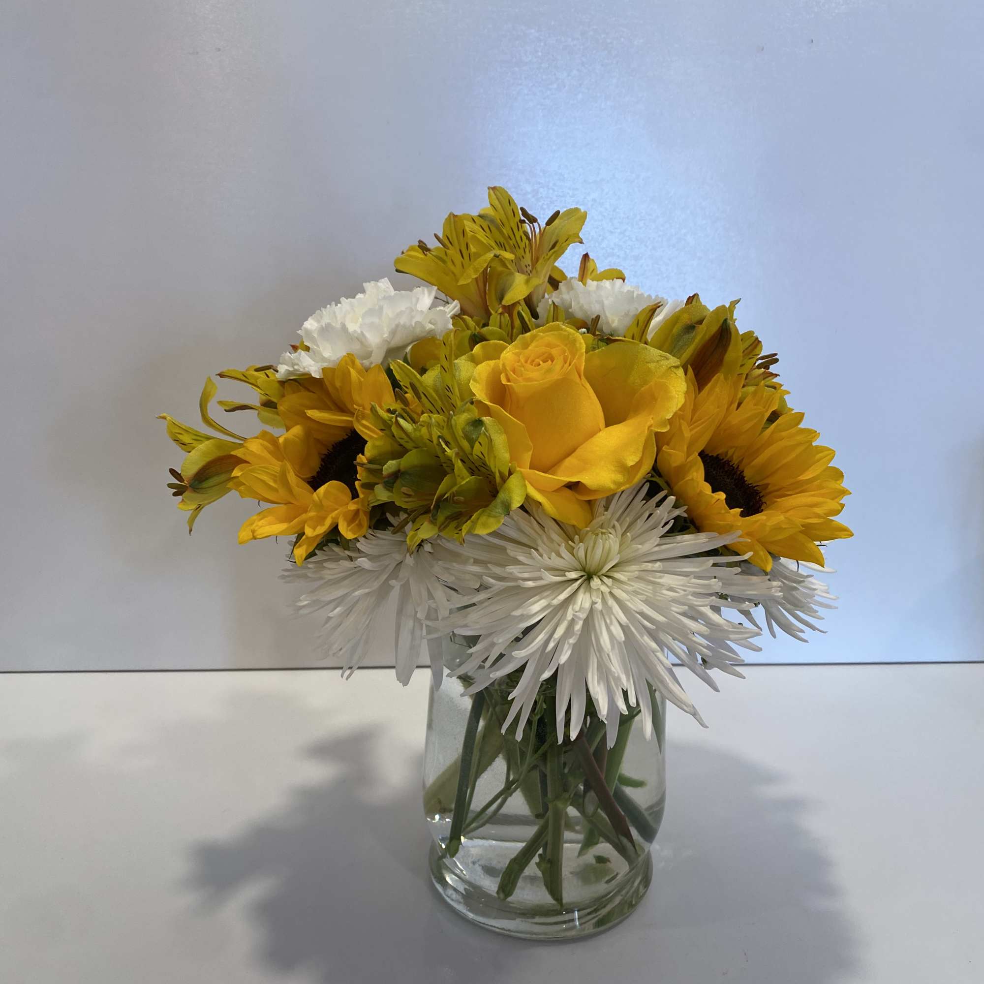 Yellow roses and sunflowers in a clear glass vase with white blooms