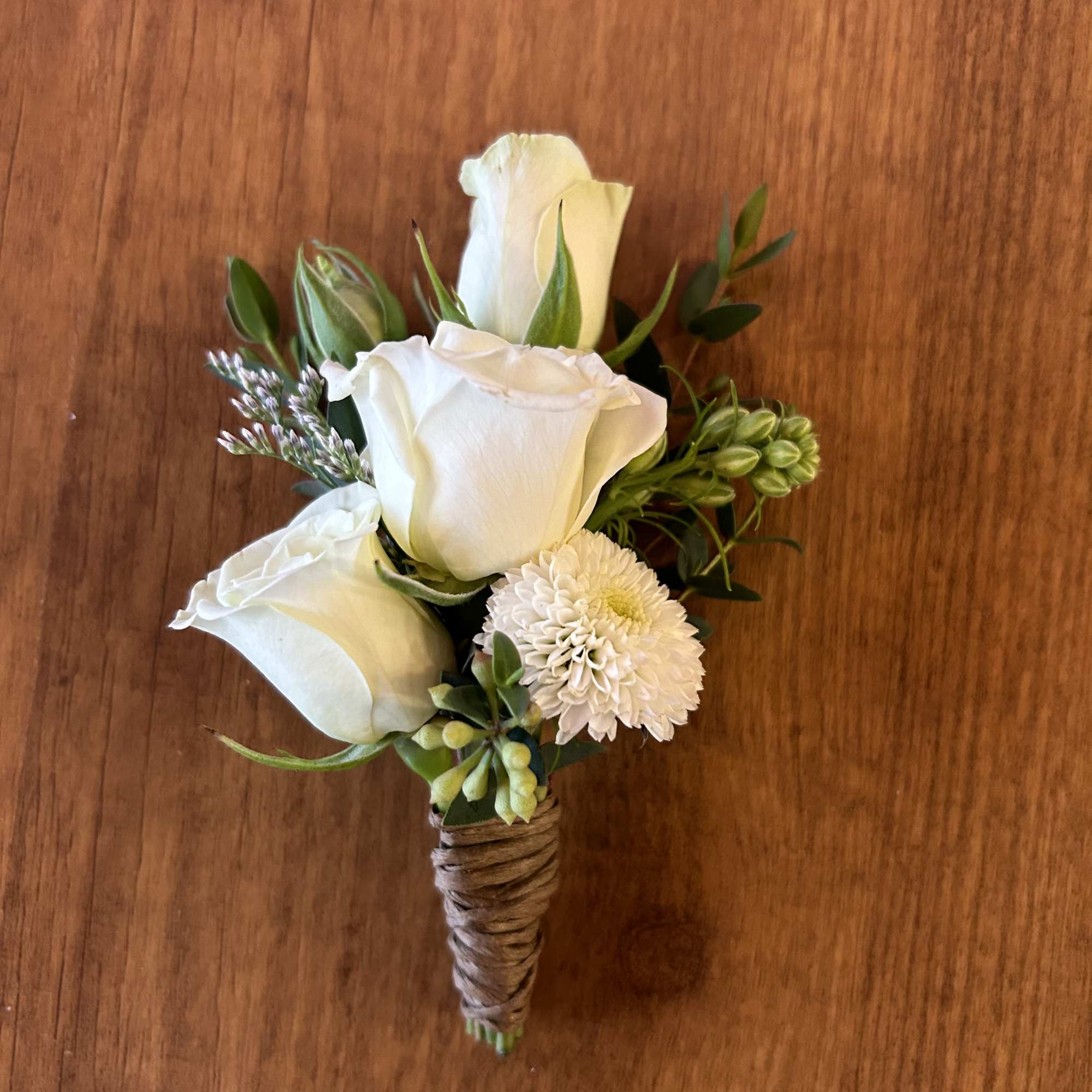 Small white rose boutonniere with greenery on a wooden surface