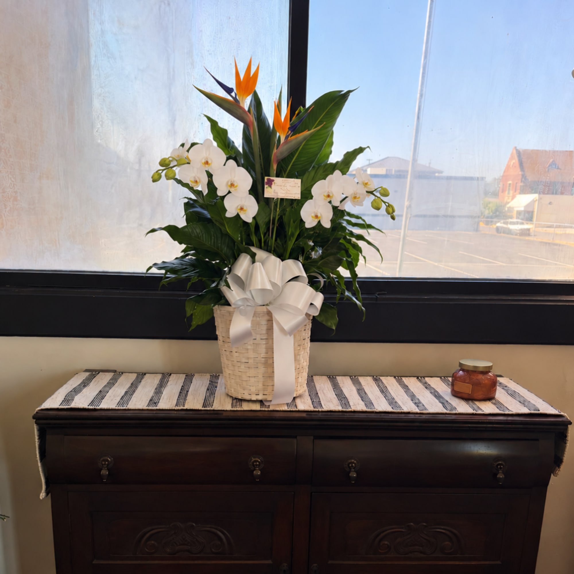 Tropical arrangement with white orchids and orange bird-of-paradise in a woven basket