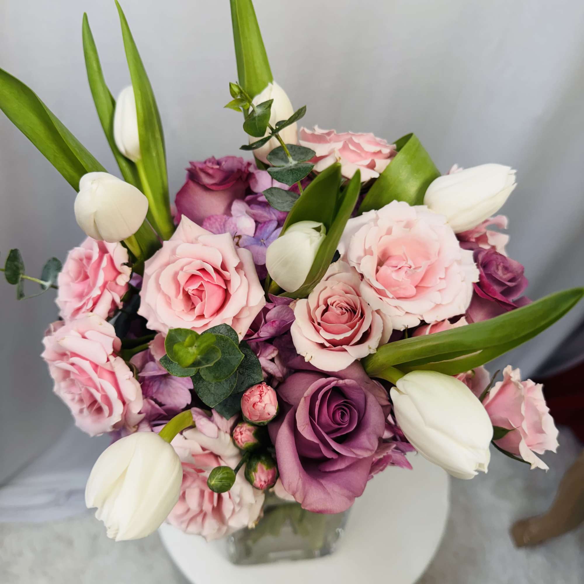 Pink and purple rose bouquet with white tulips in a glass vase