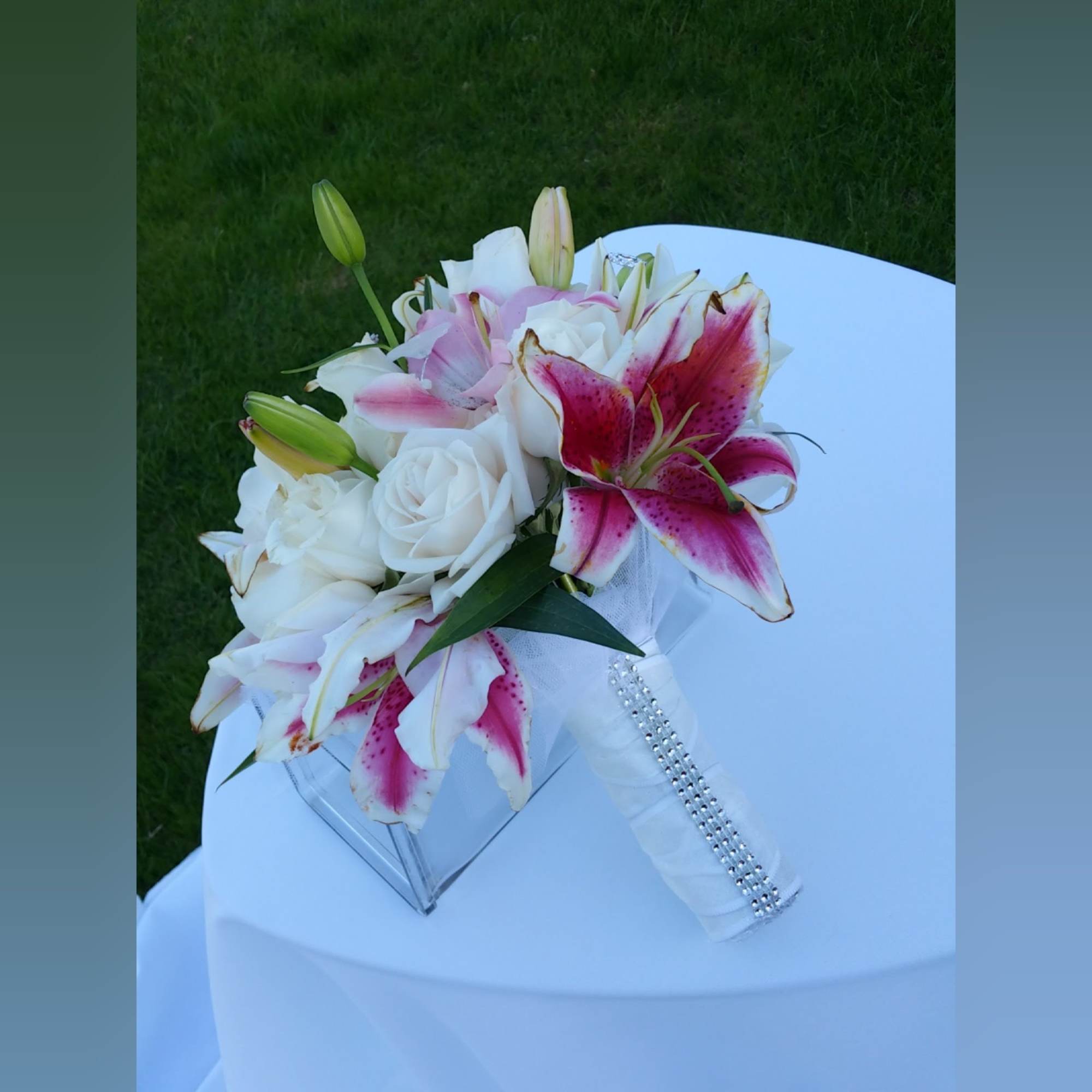 White roses and pink stargazer lilies in a clear vase with a jeweled handle