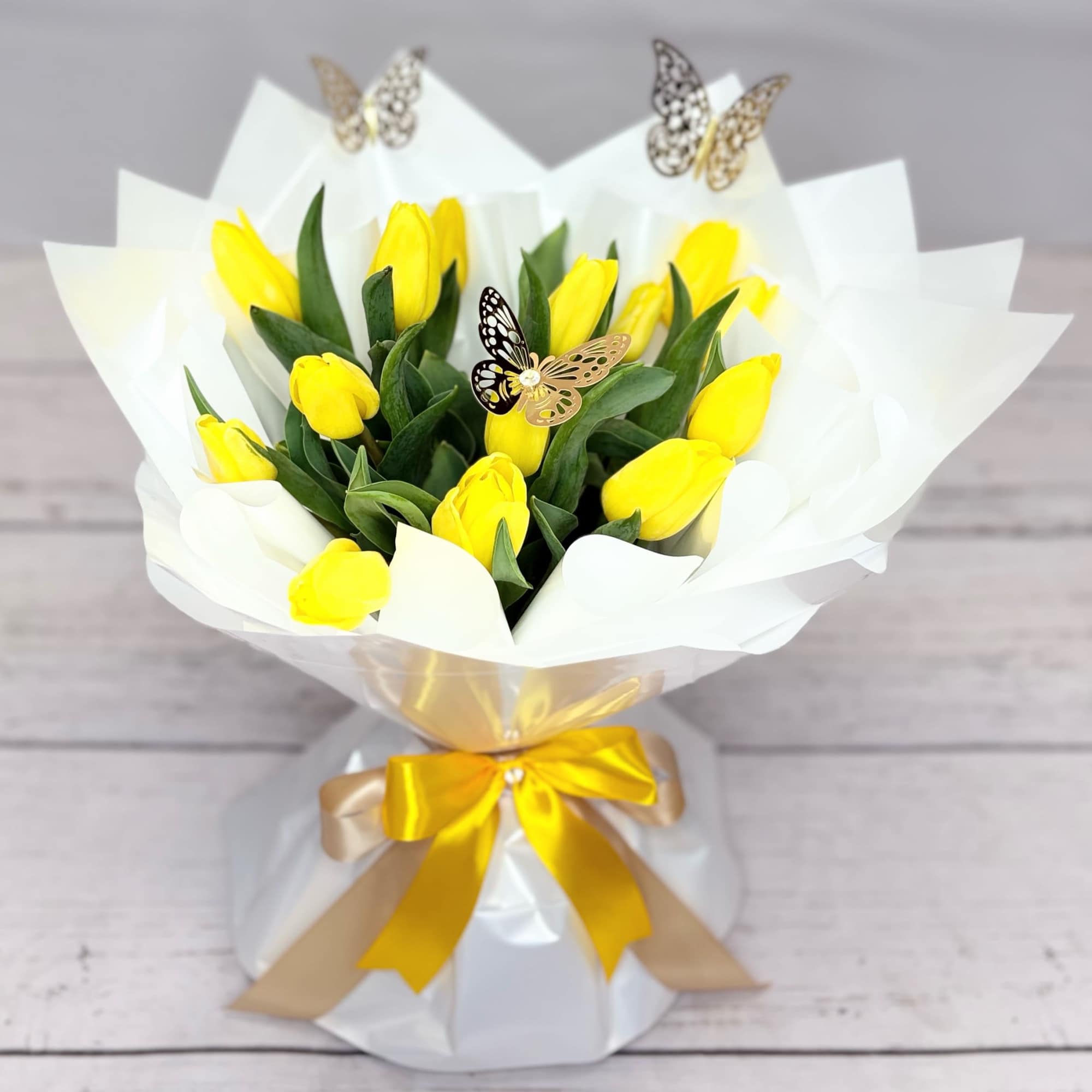 Yellow tulip bouquet wrapped in white paper with a gold ribbon