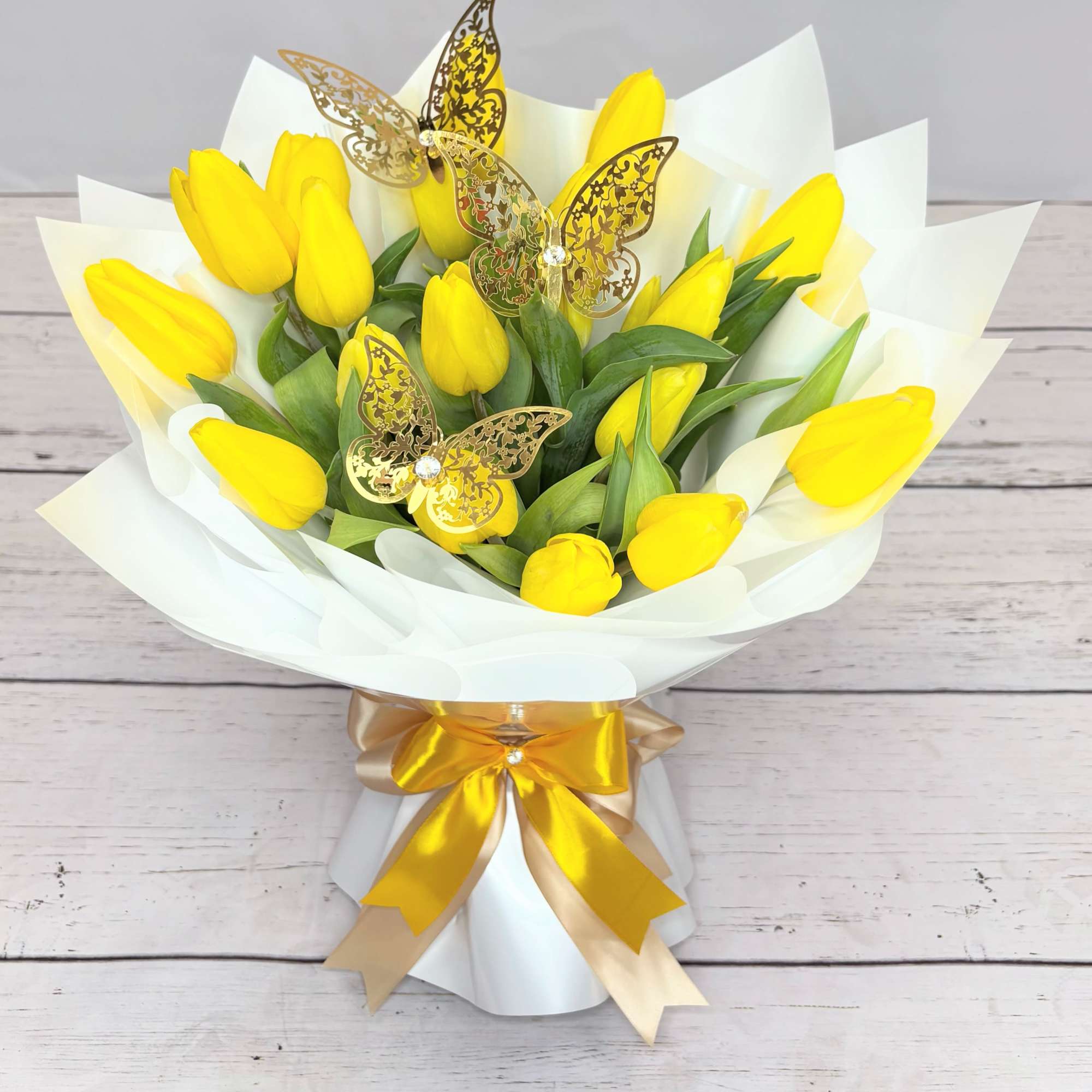 Bouquet of yellow tulips wrapped in white paper with a gold ribbon