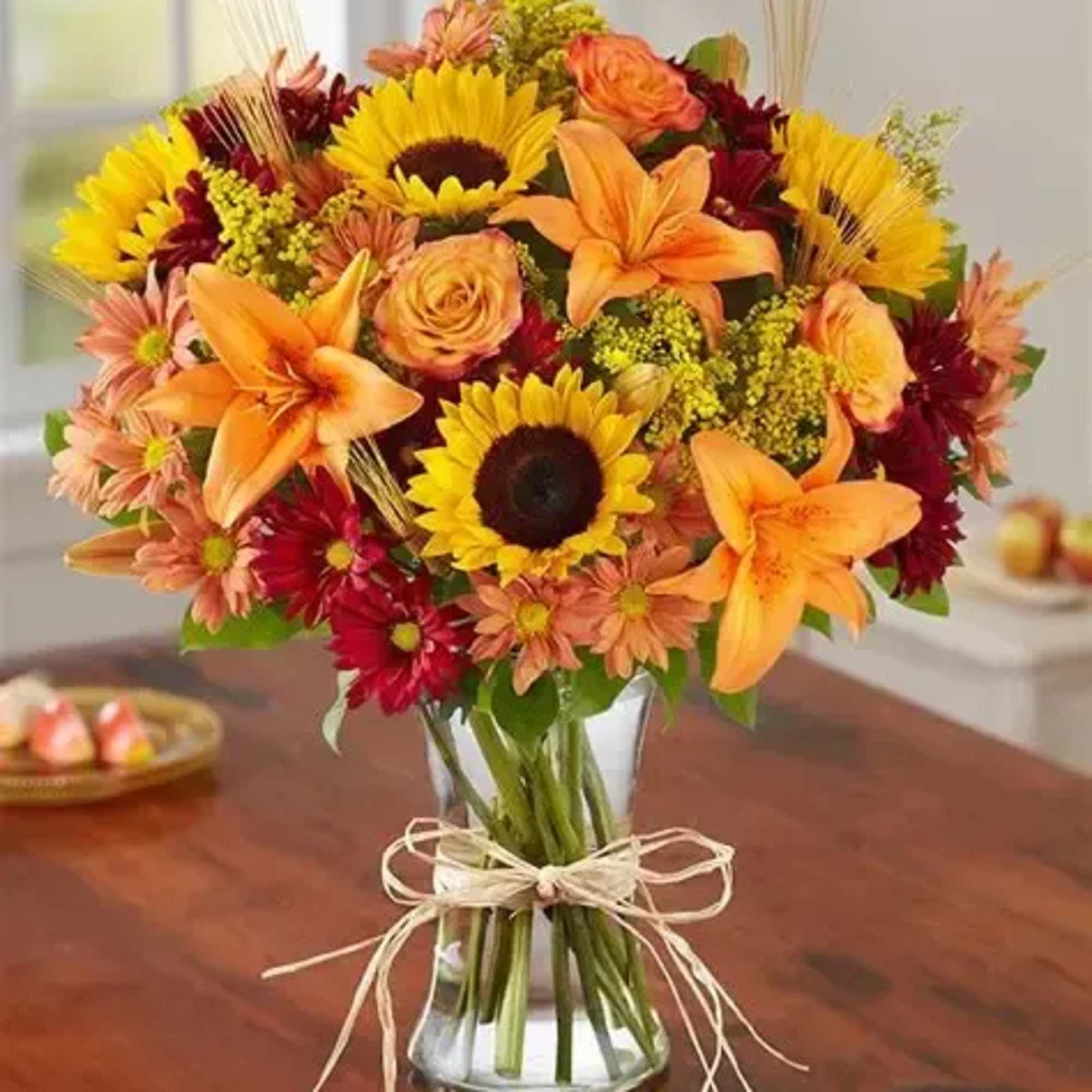 Bouquet of sunflowers, orange lilies, and mixed daisies in a glass vase