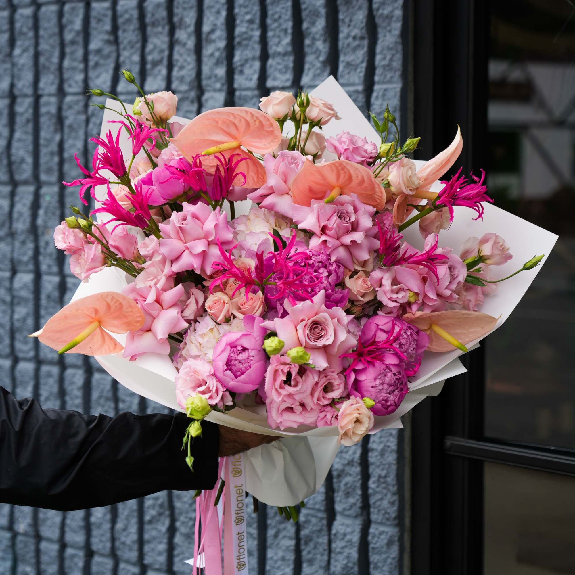 Pink and peach bouquet with anthuriums, roses, and lisianthus wrapped in white paper