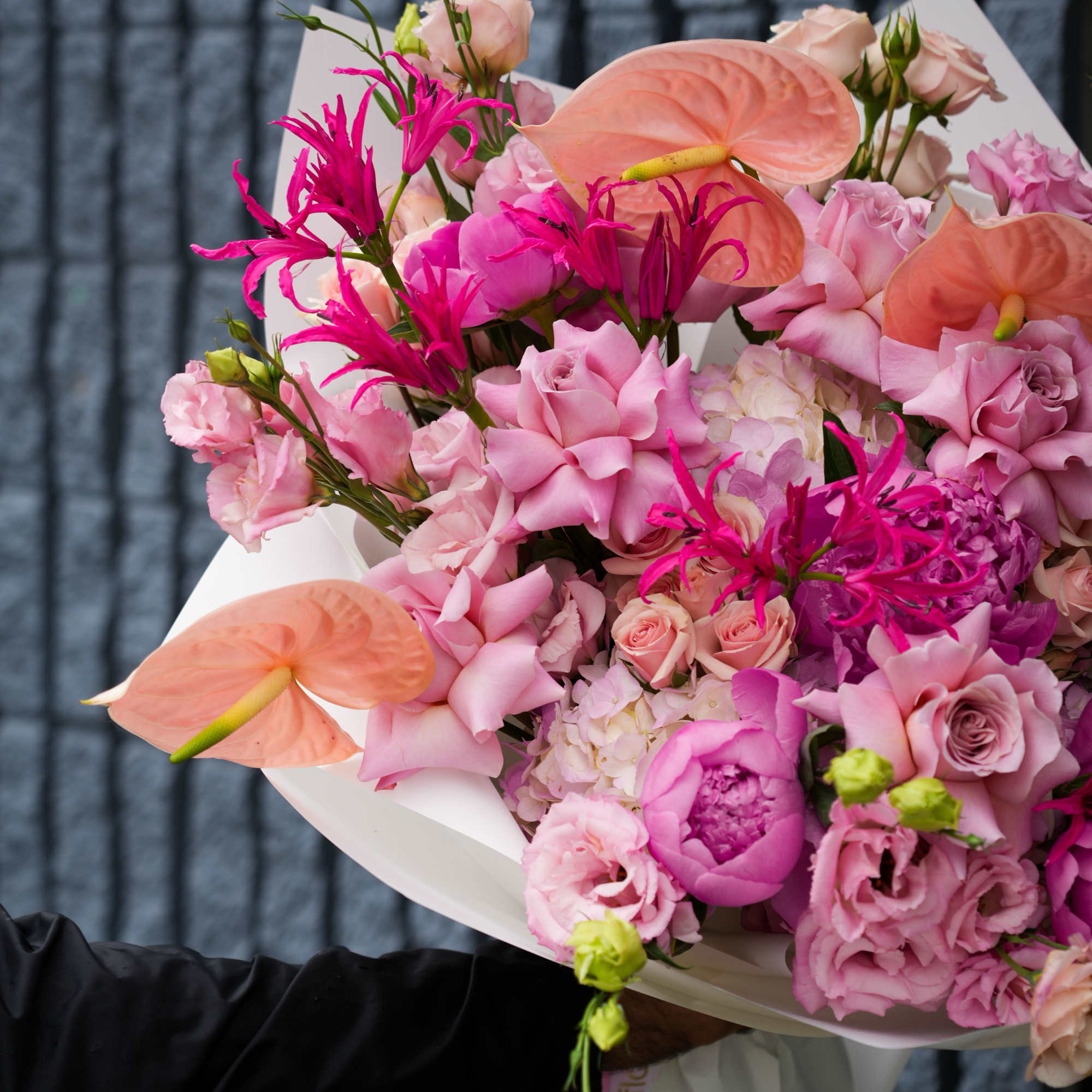Pink bouquet with anthuriums, roses, and lisianthus wrapped in white paper