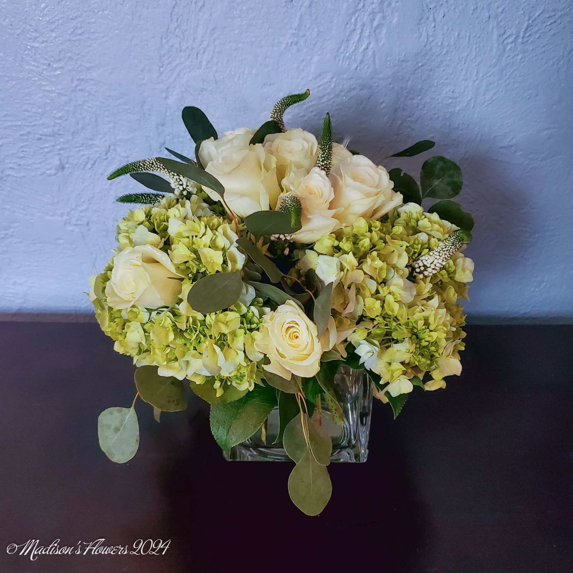 Classic round table-top arrangement featuring cream colored roses, accent flowers in soft