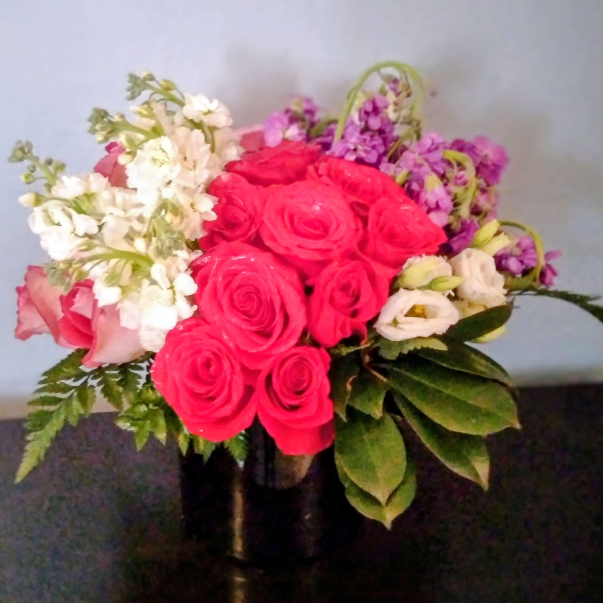 Bouquet of pink roses, white blooms, and purple flowers in a dark vase