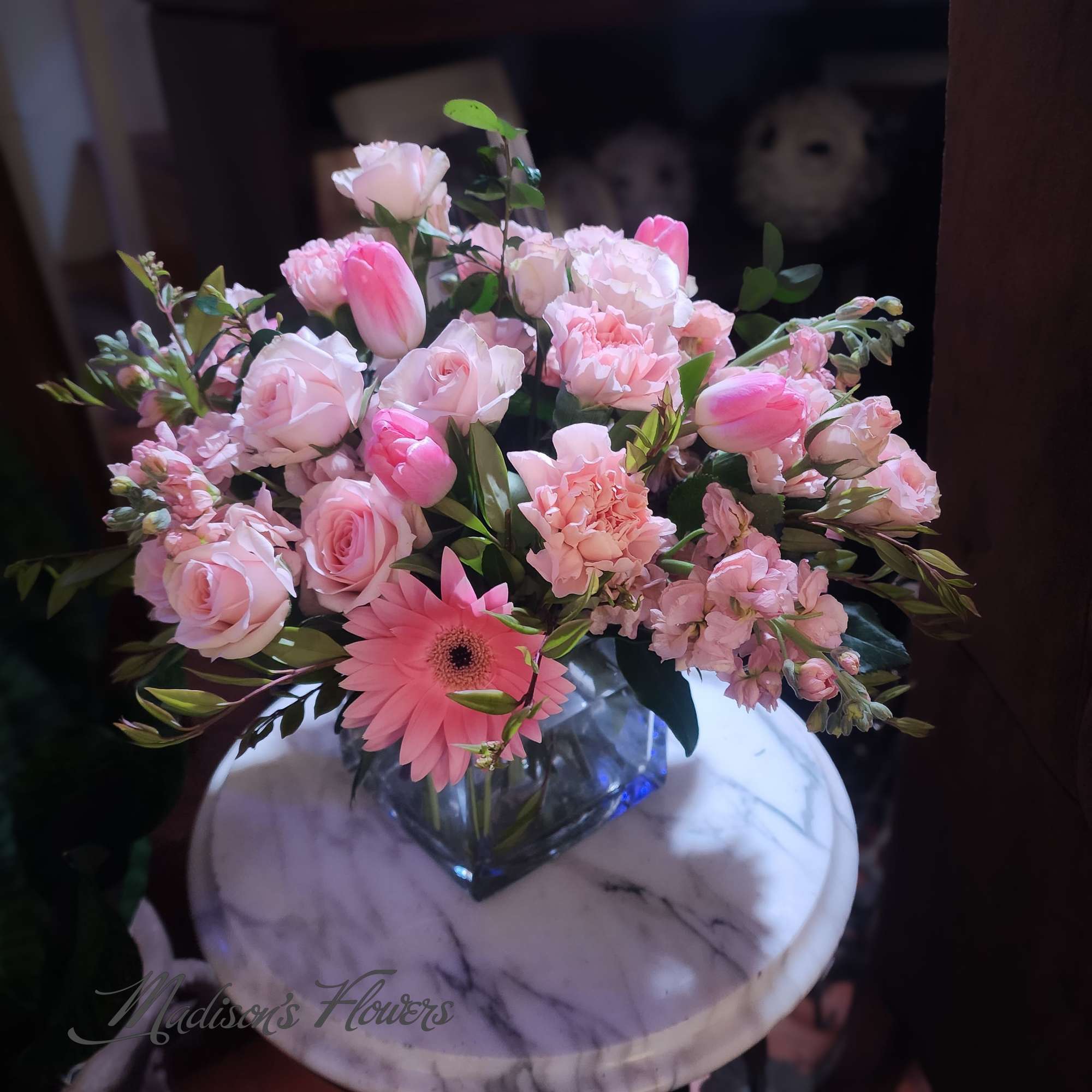 Low arrangement of pink roses, tulips, carnations, and a gerbera daisy in a glass cube vase.