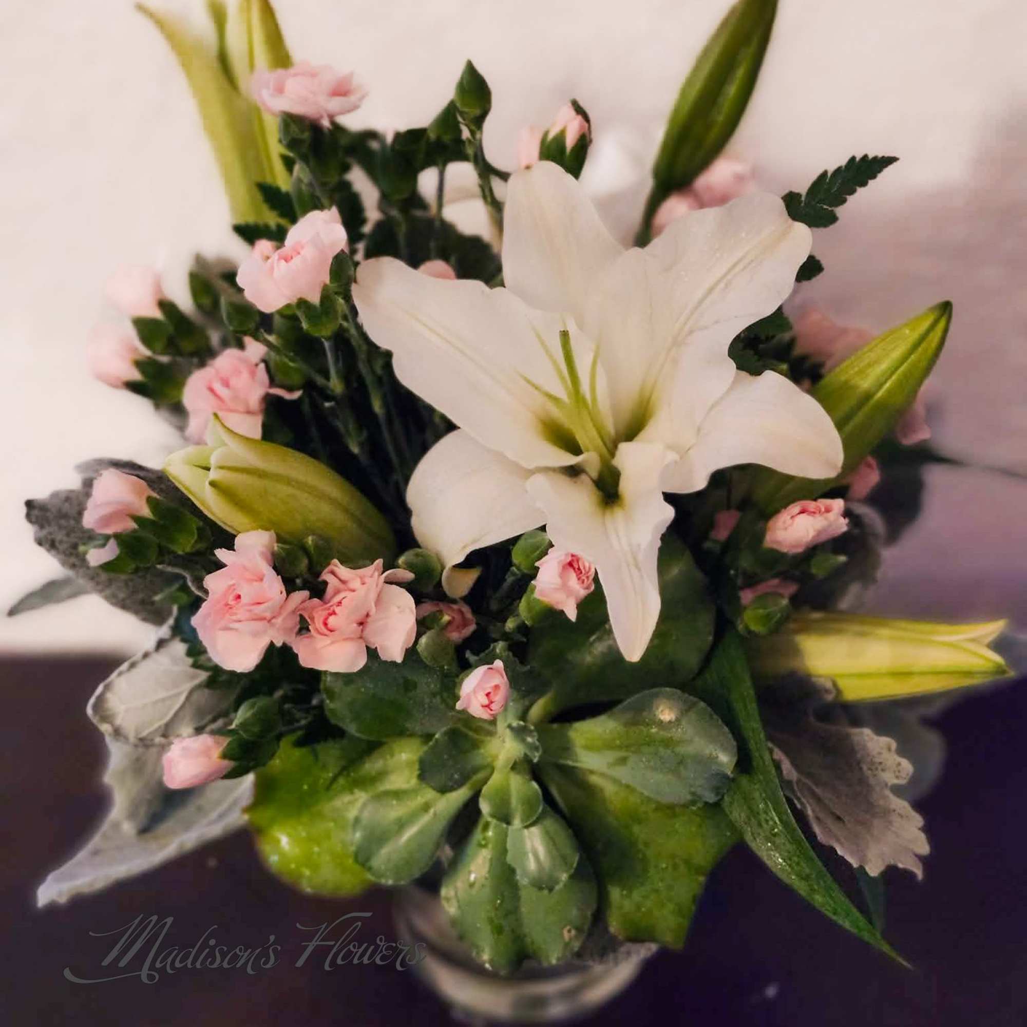White lily bouquet with pink carnations in a glass vase