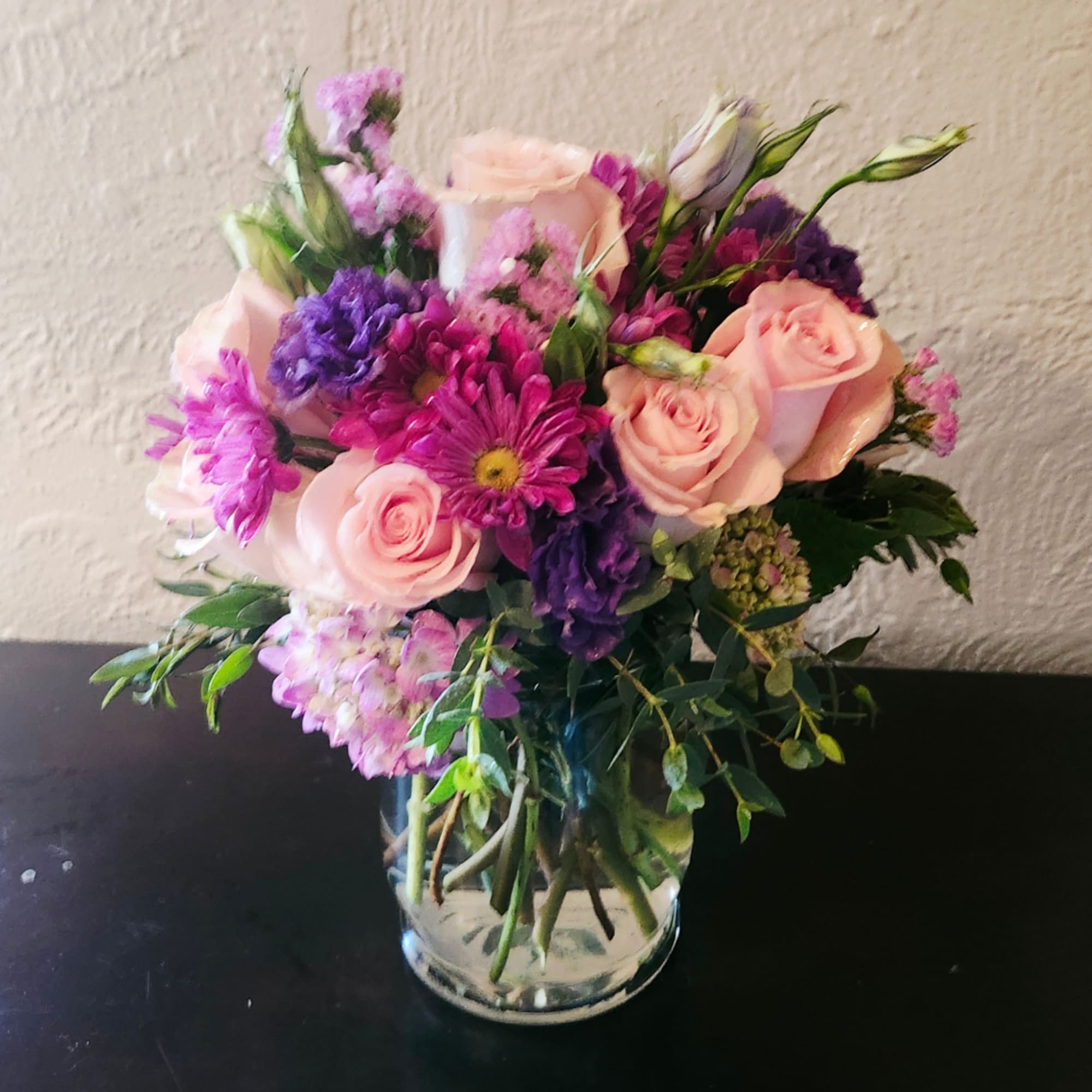 Pink roses and purple mixed flowers in a clear glass vase