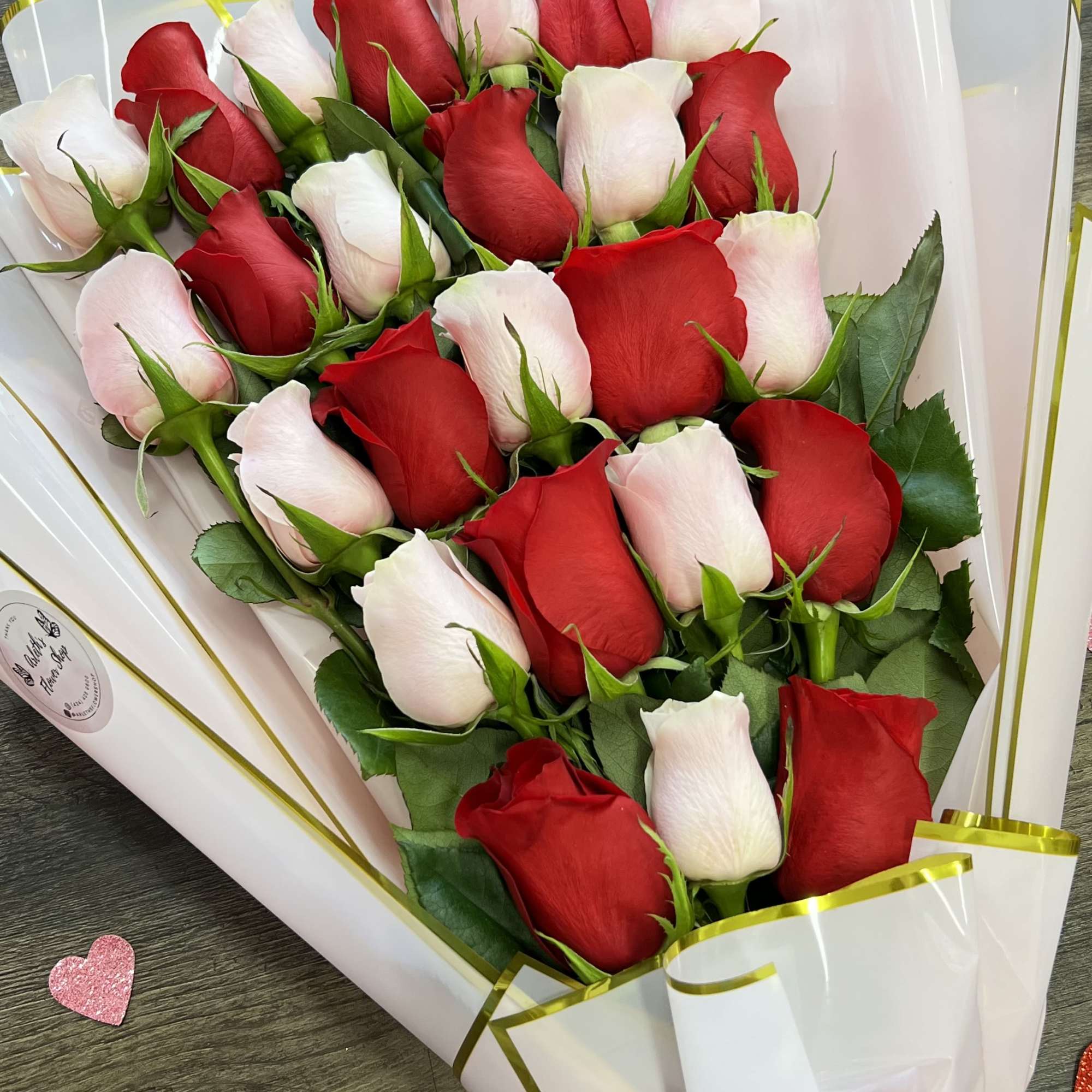 Bouquet of red and pale pink roses wrapped in white paper with a red bow.