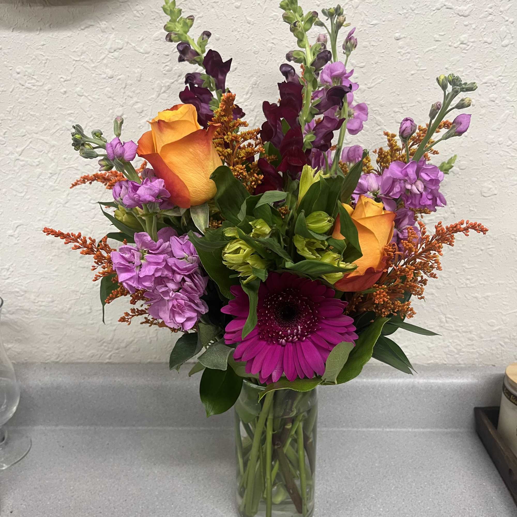 Mixed bouquet in a clear glass vase with orange roses and purple blooms