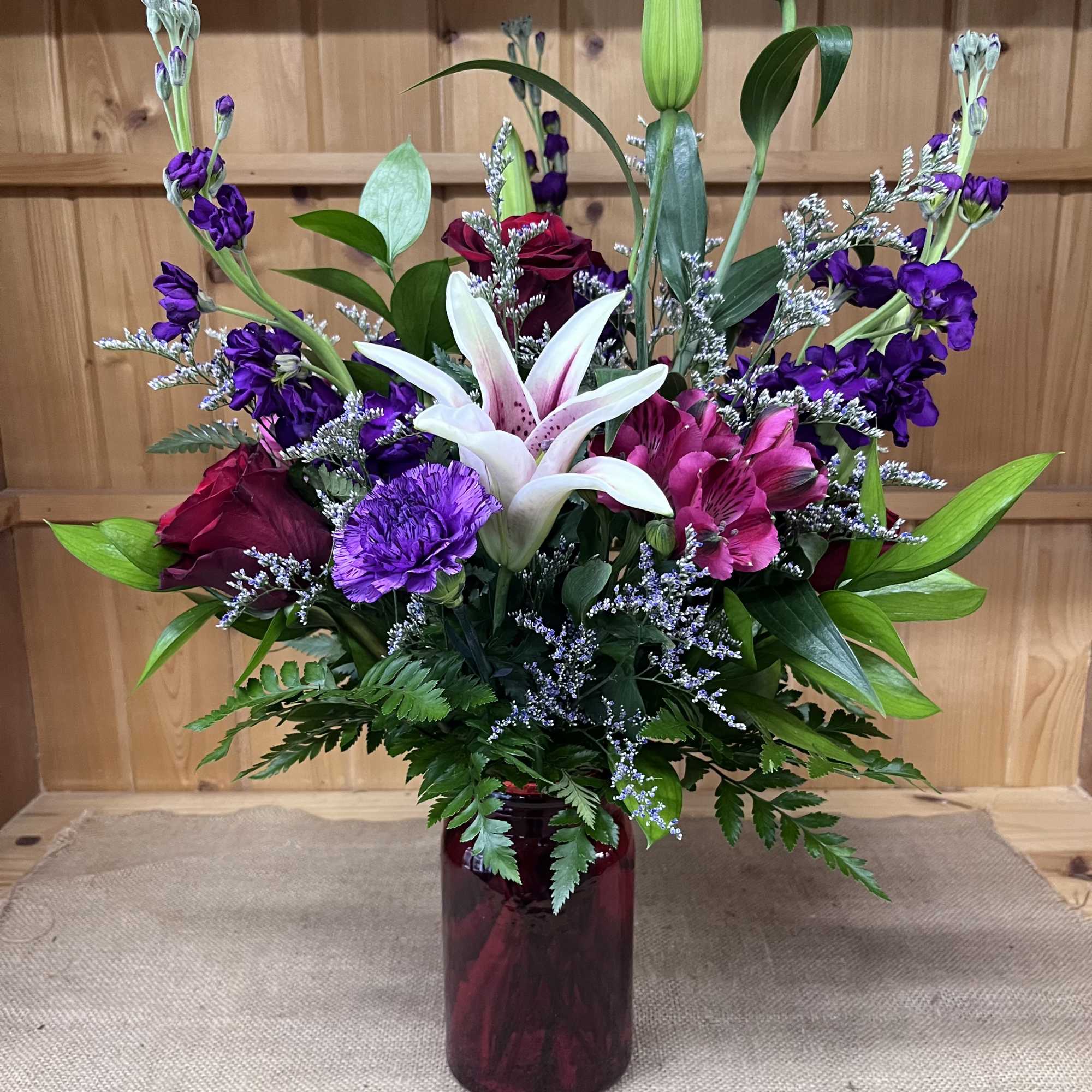 Mixed bouquet with lilies, roses, and purple flowers in a burgundy vase