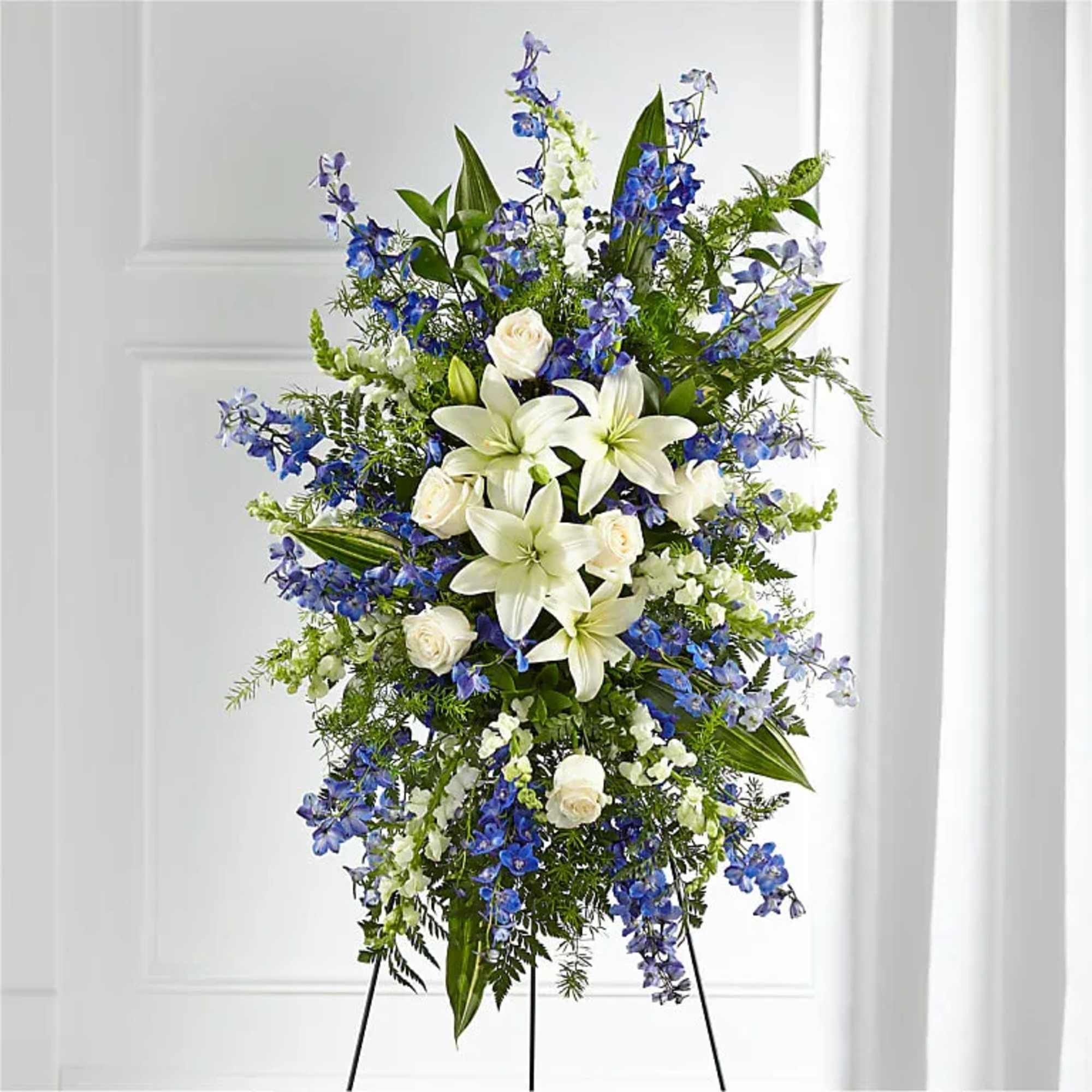 Standing floral spray with white lilies, white roses, and blue flowers