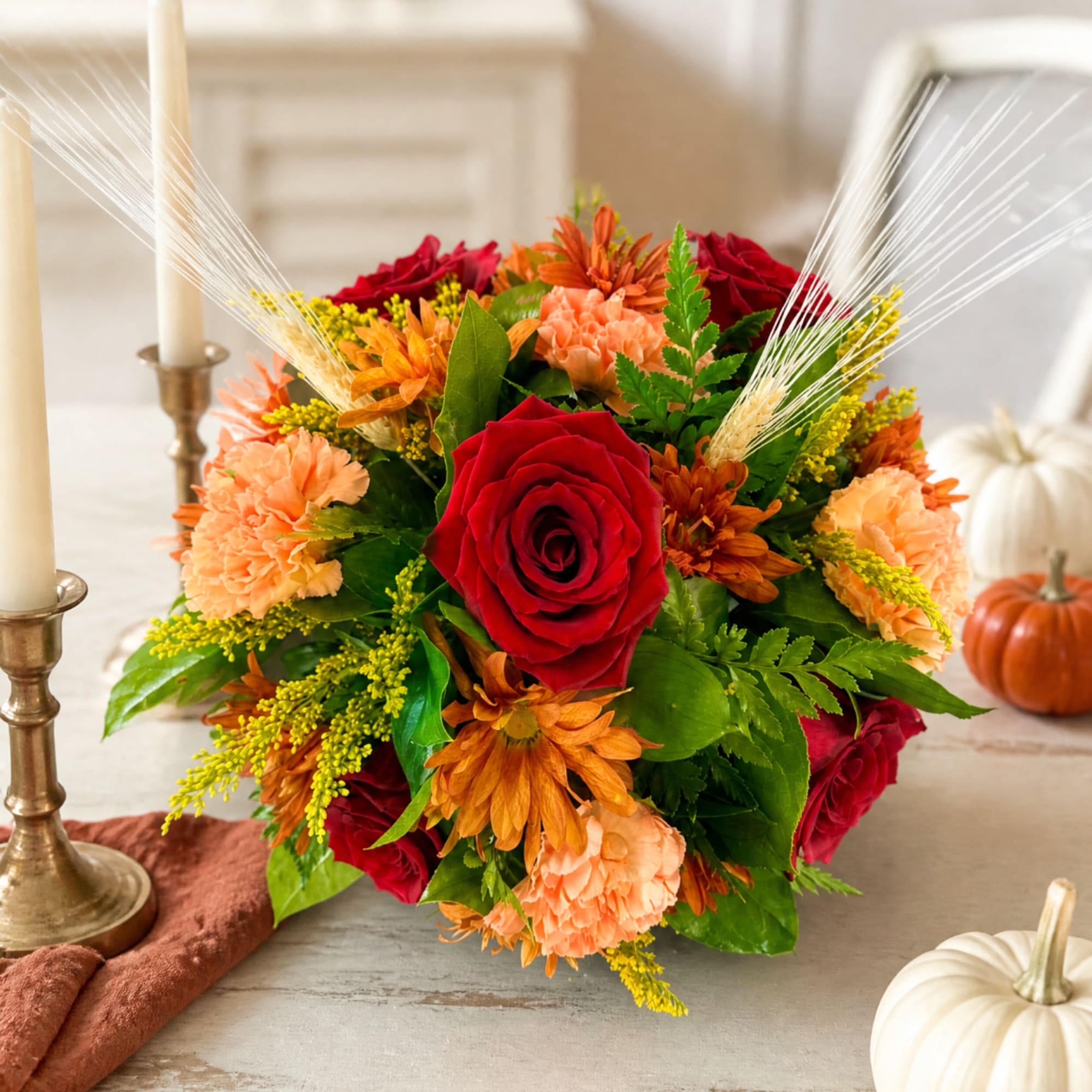 Bouquet of red roses, peach carnations, and orange flowers with wheat accents
