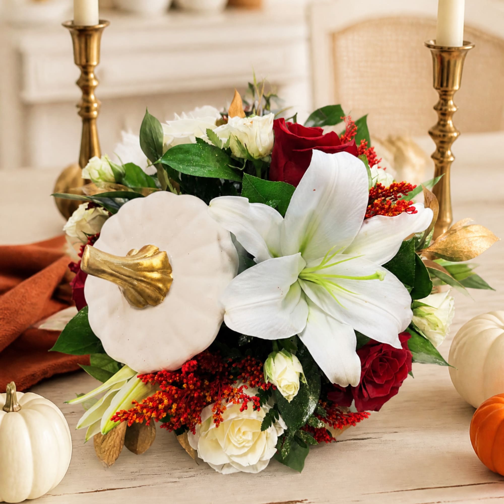White lilies and red roses arranged with pumpkins and candles