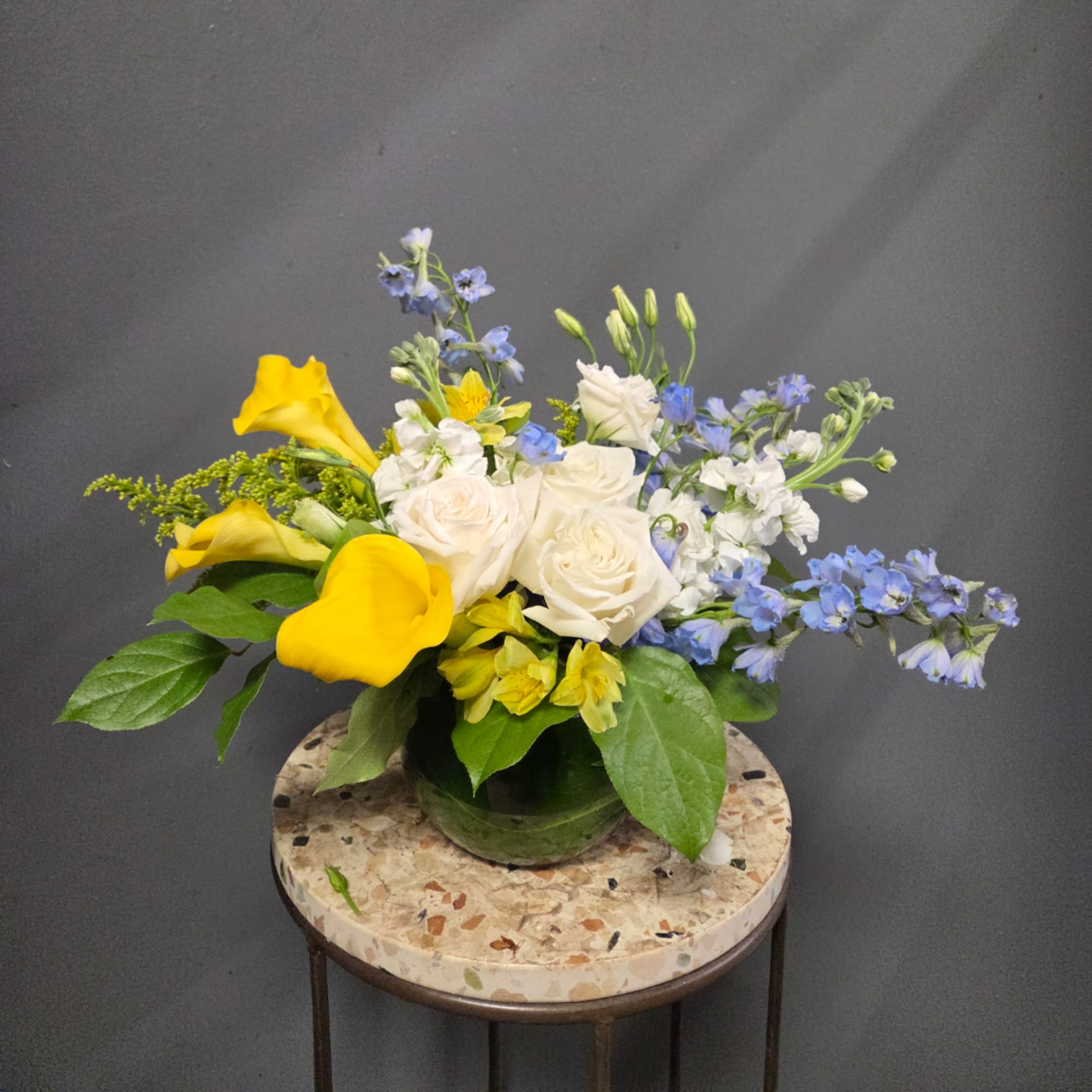 Yellow calla lilies and white roses in a glass vase with blue flowers