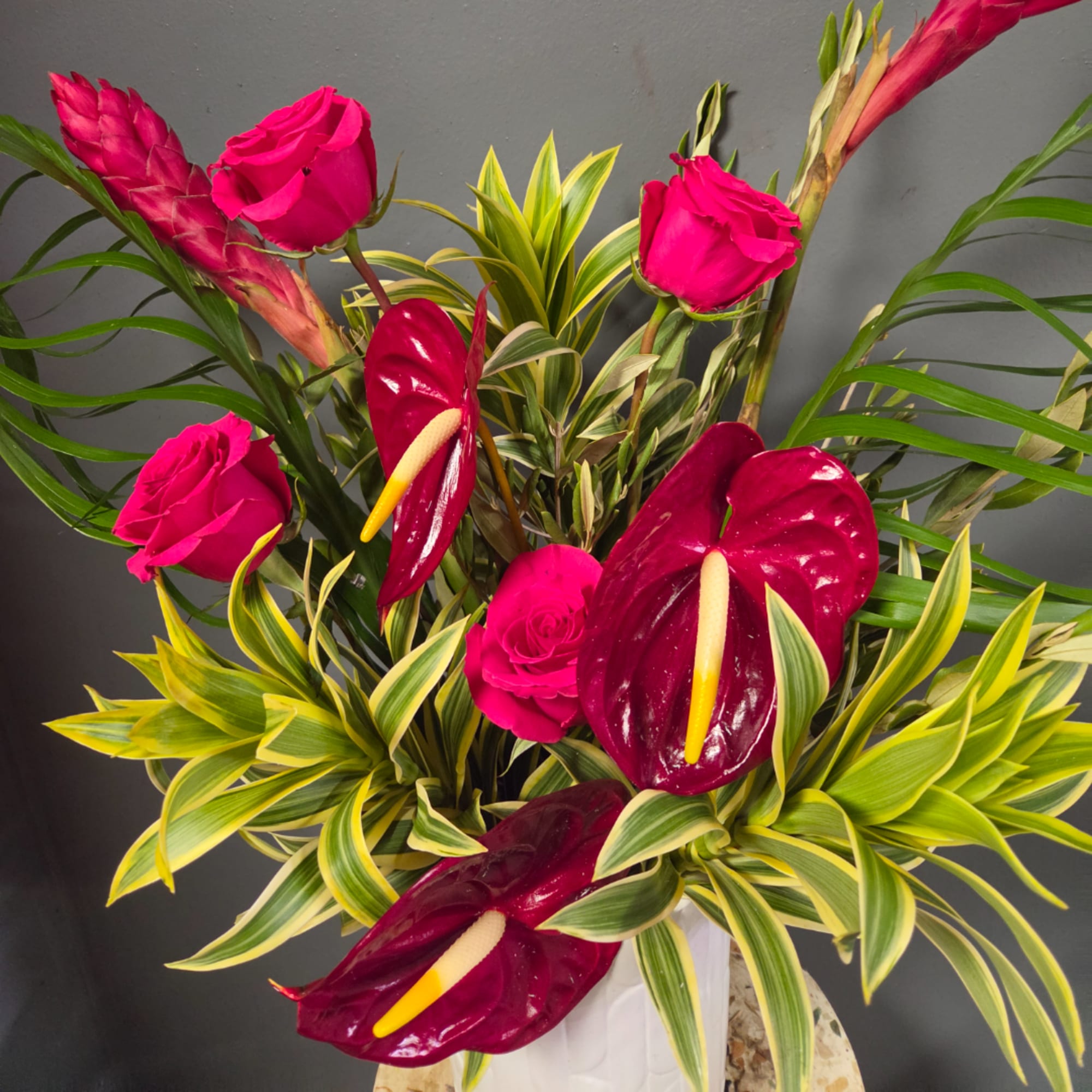 Pink roses and burgundy anthuriums in a white vase with variegated foliage, photo 2 of 5