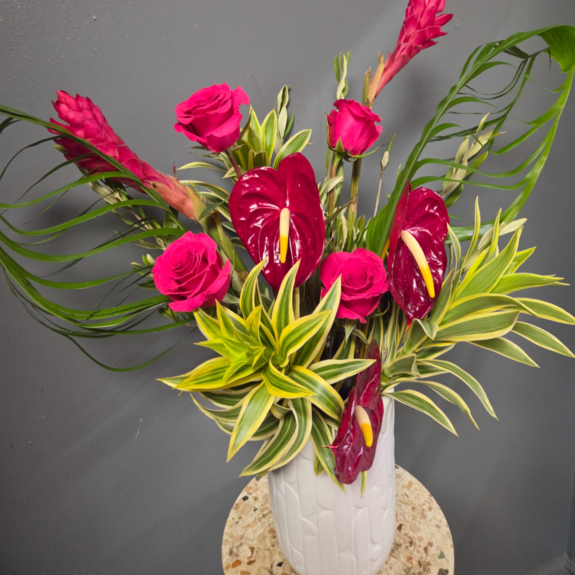 Pink roses and burgundy anthuriums in a white vase with variegated foliage, photo 4 of 5
