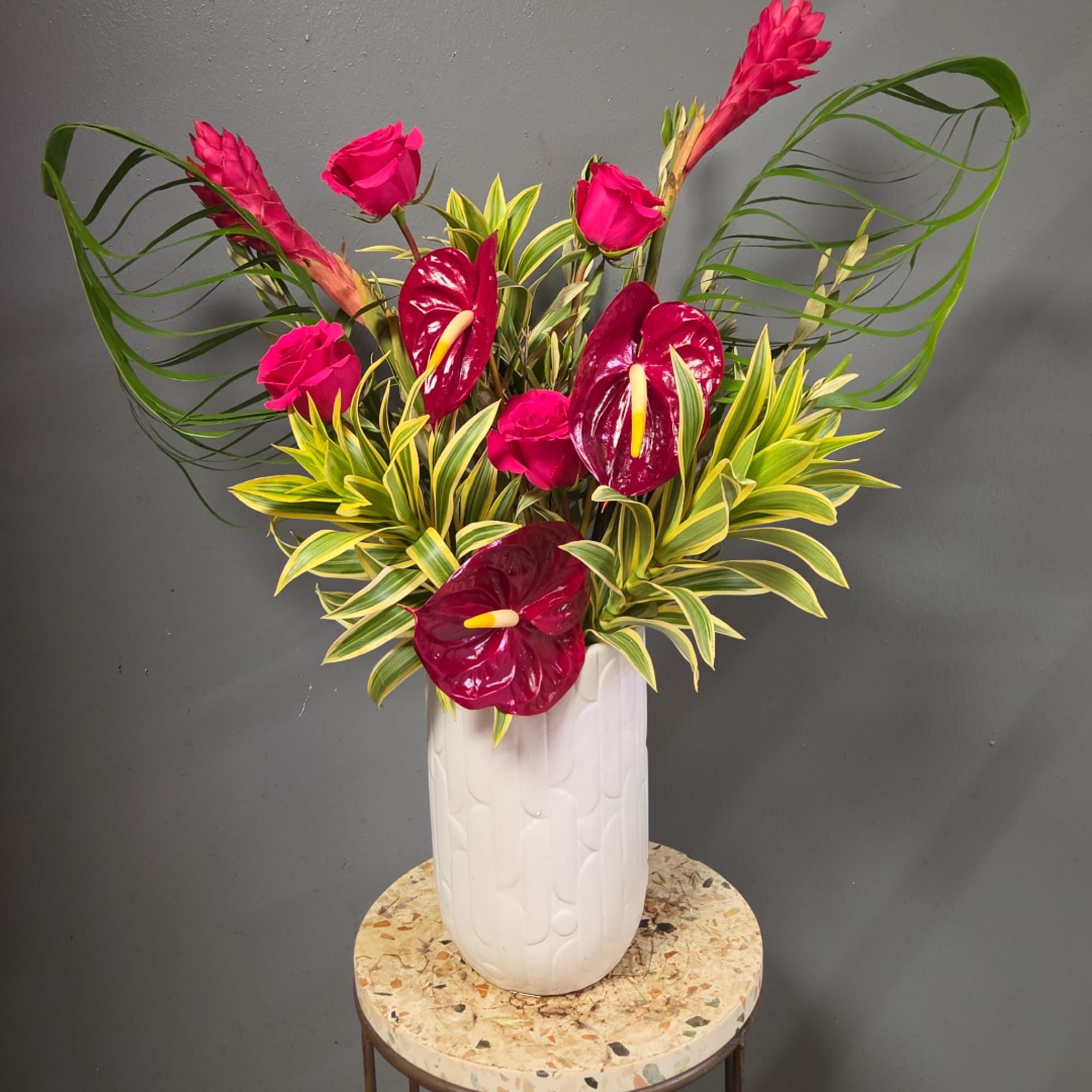 Tropical arrangement with magenta anthuriums and pink roses in a white vase