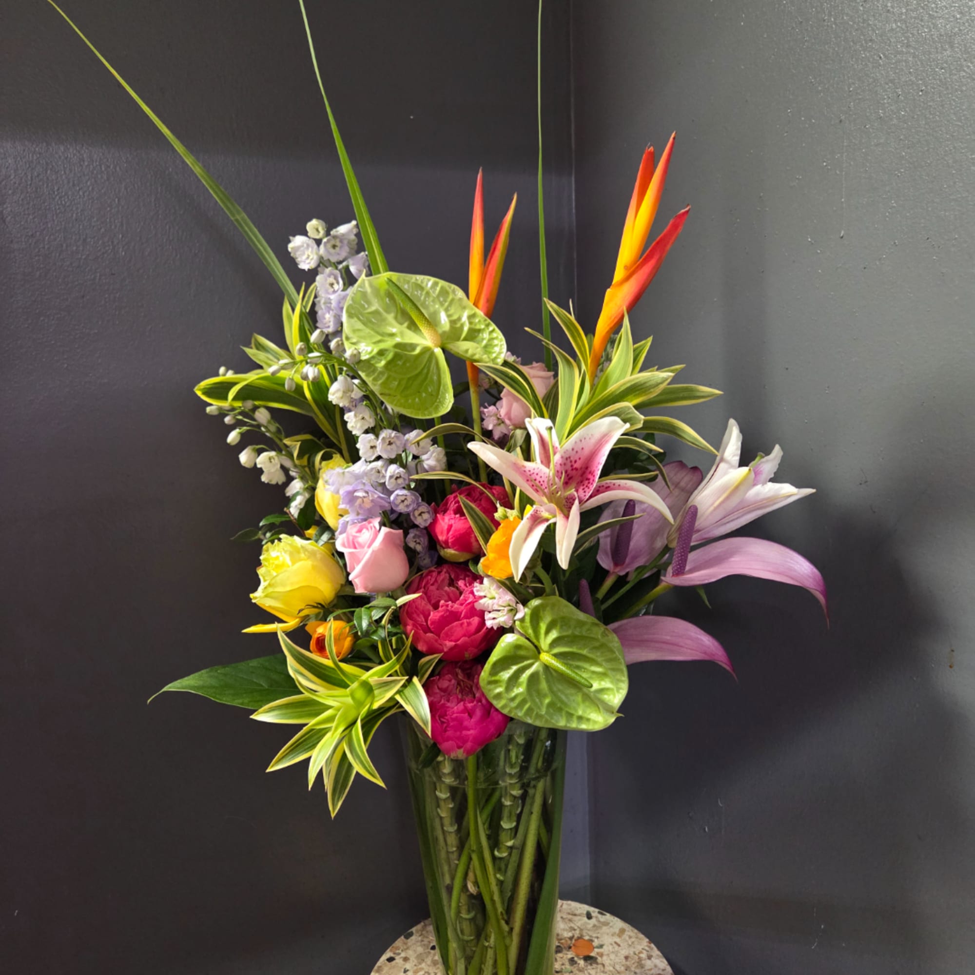 Colorful tropical bouquet in a tall glass vase with lilies and roses