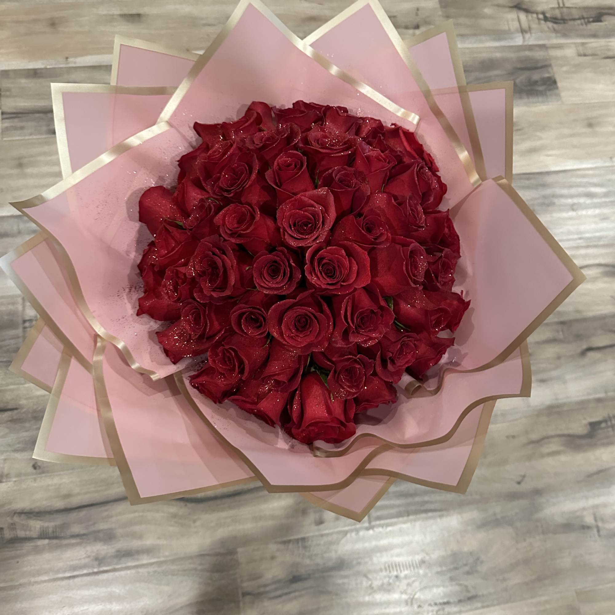 A bouquet of red roses wrapped in pink paper with gold trim.