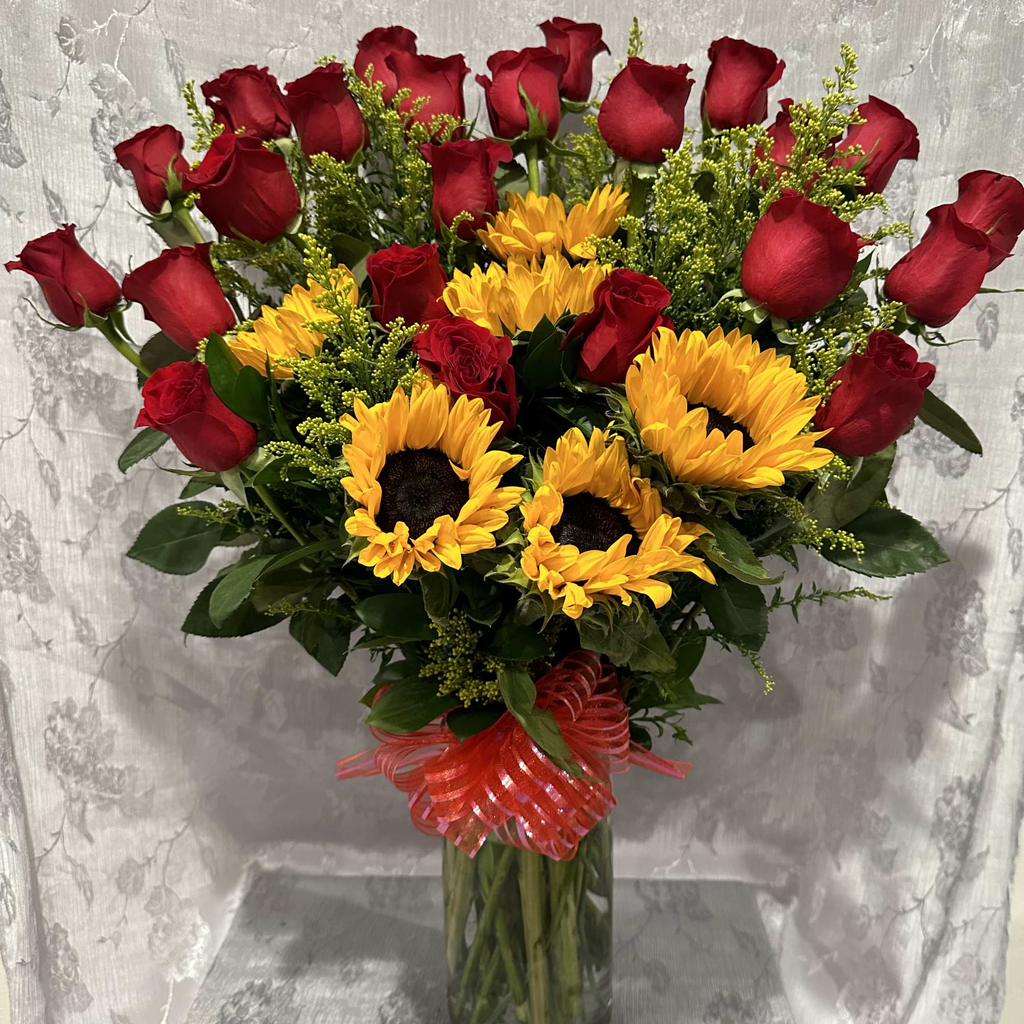 Red roses and yellow sunflowers in a glass vase with a red ribbon