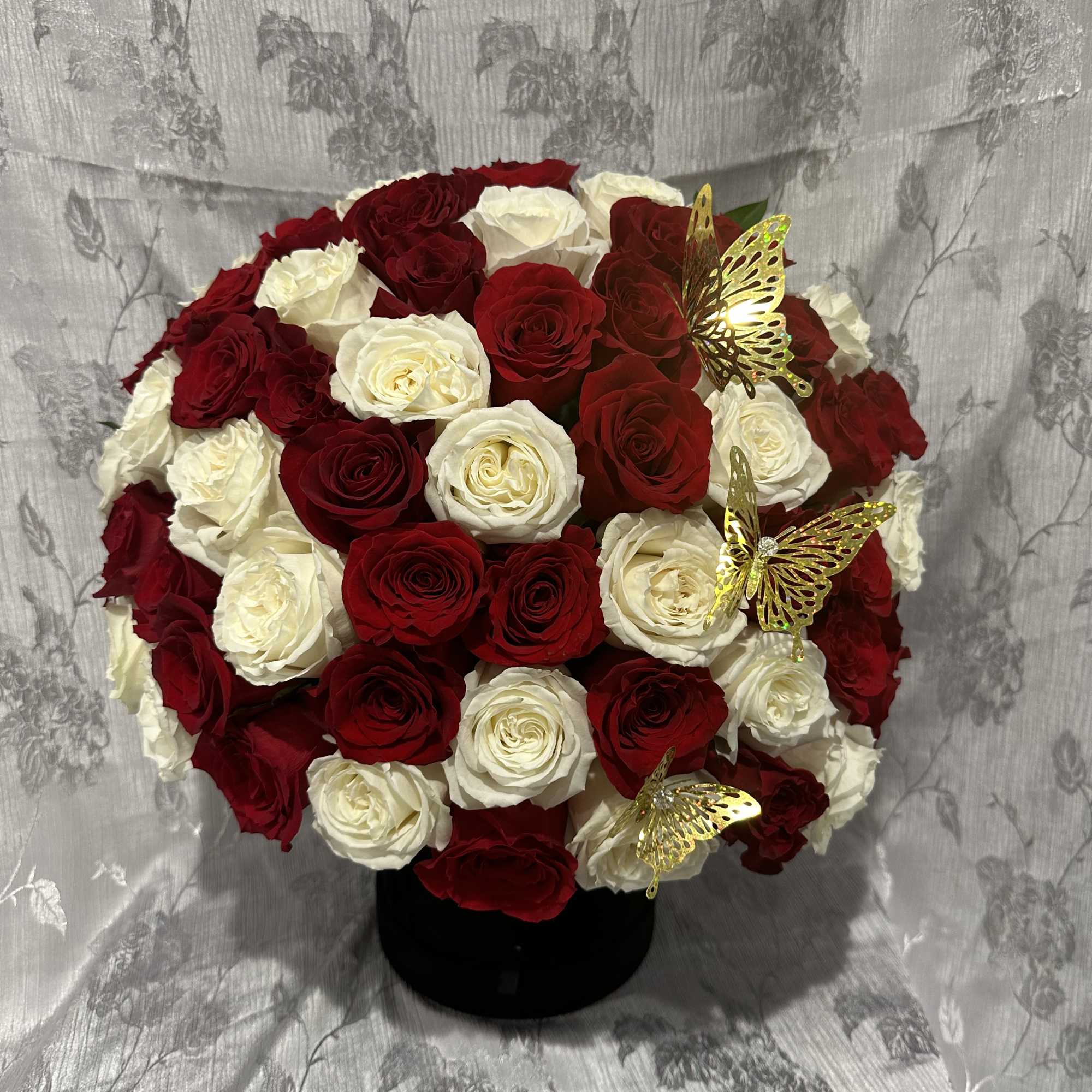Red and white rose arrangement in a black vase with gold butterfly accents
