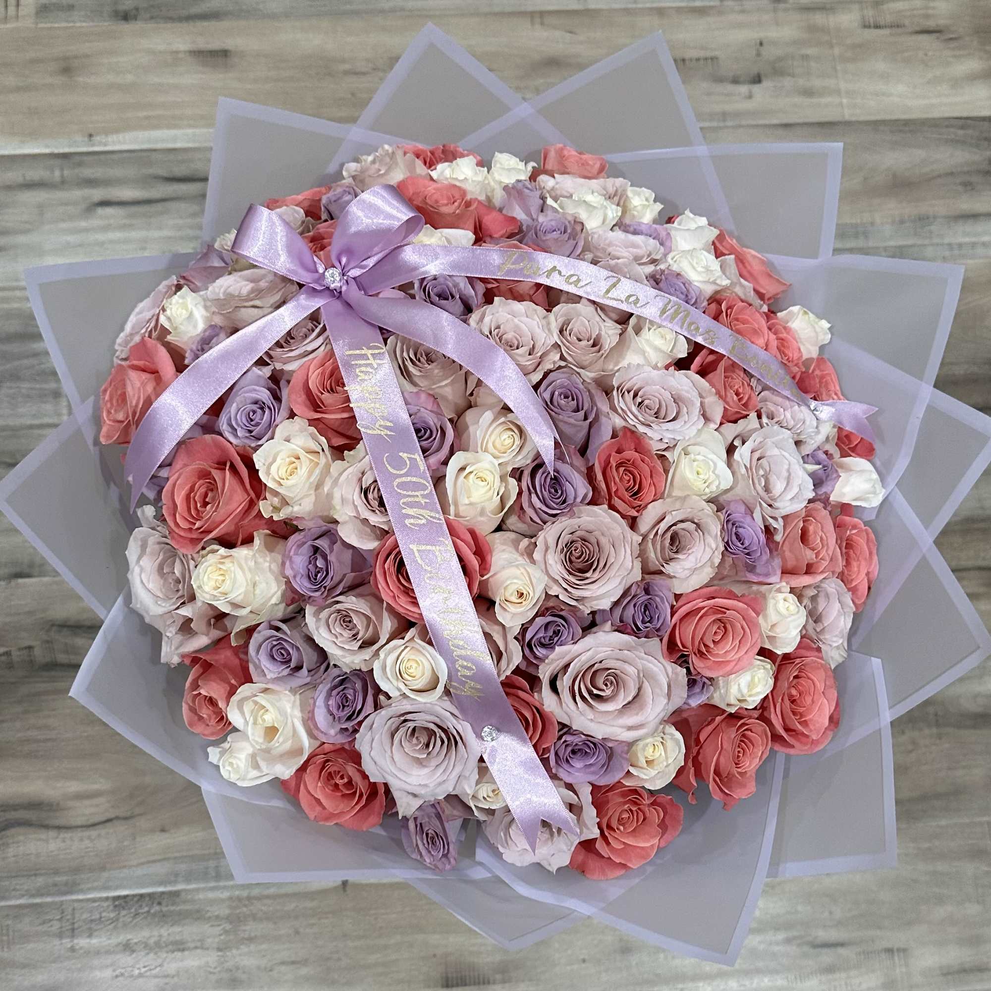 Round bouquet of pink, lavender, and white roses with a lavender ribbon