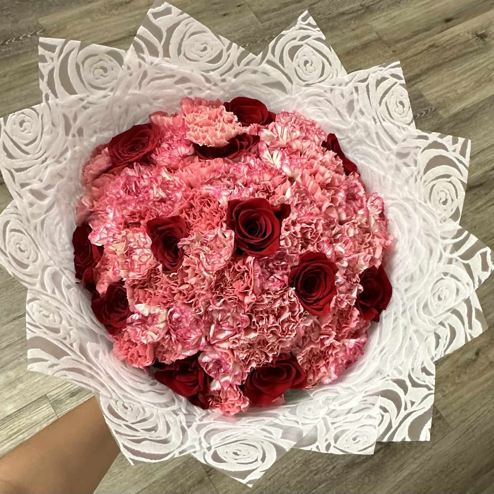 Pink carnation bouquet with red roses wrapped in white patterned paper