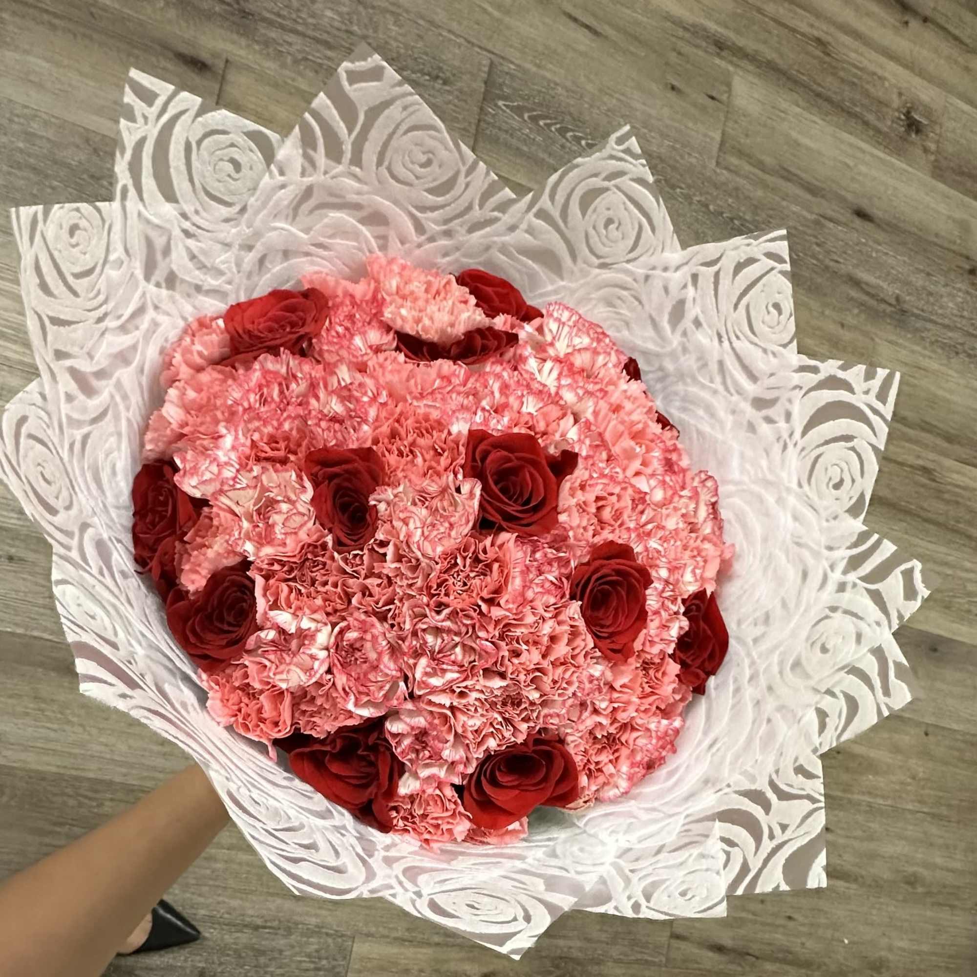 Round bouquet of pink carnations and red roses wrapped in white paper
