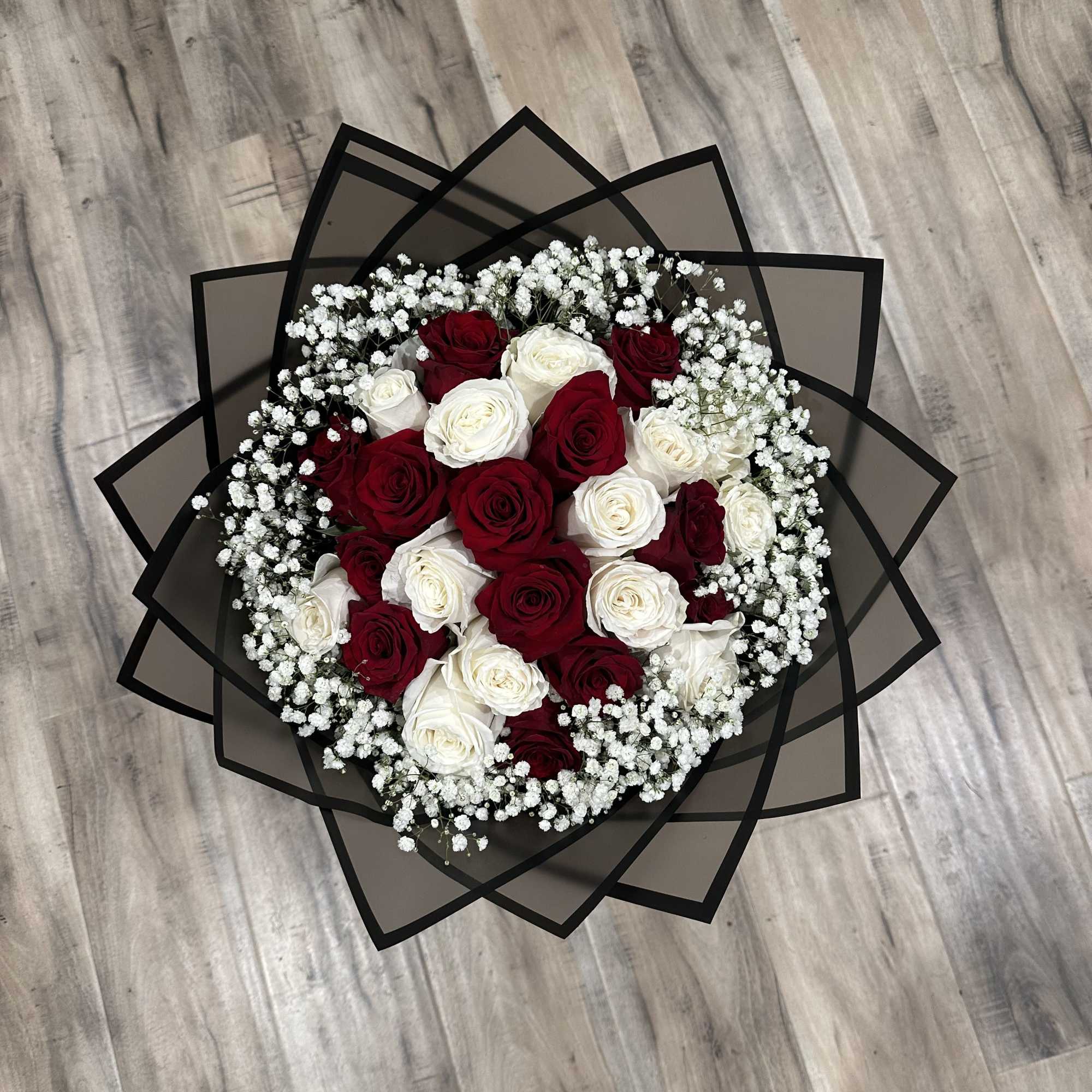 Round bouquet of red and white roses with baby's breath in black wrap