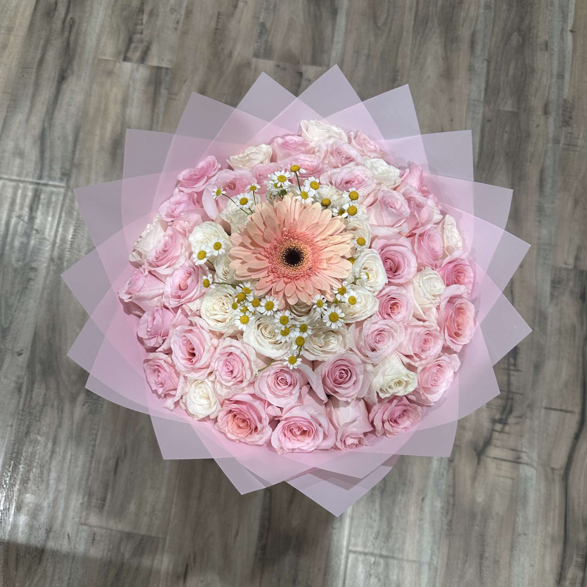 Round bouquet of pink and white roses with a peach gerbera daisy center