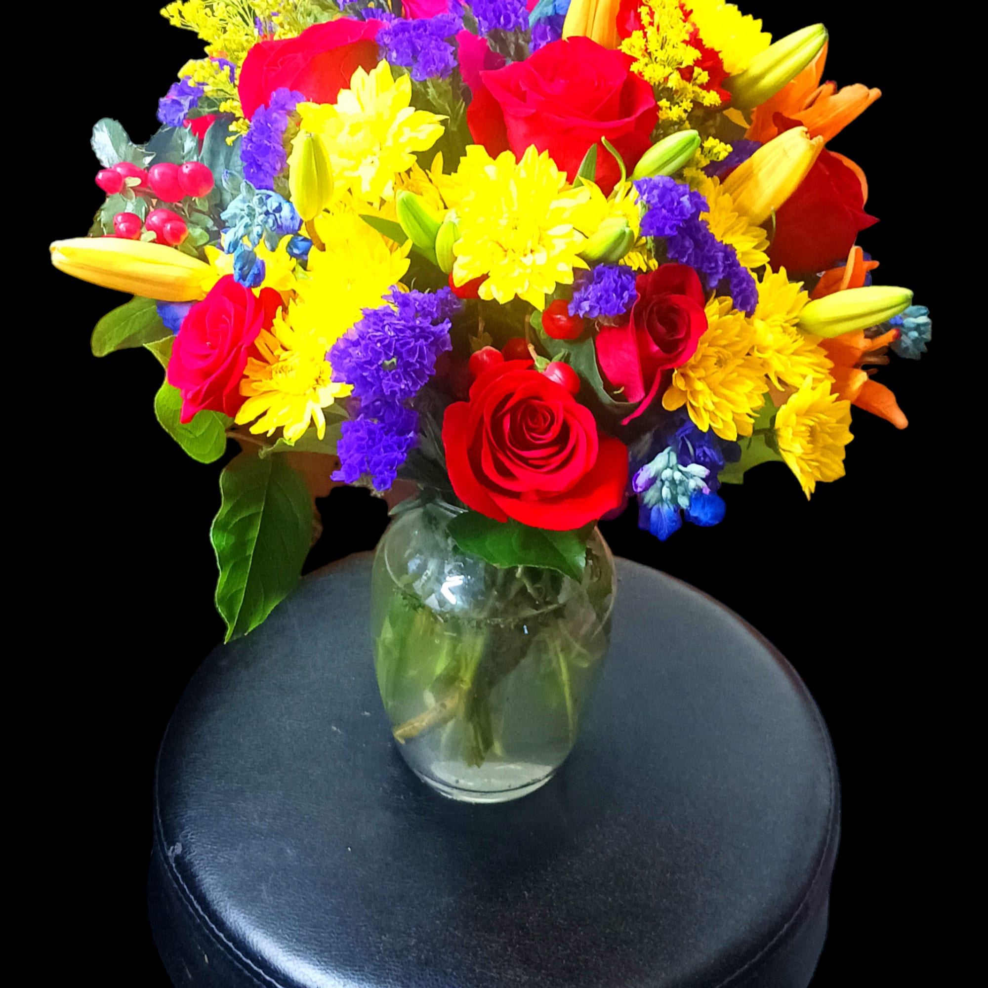 Bright mixed bouquet of roses, lilies, and daisies in a glass vase