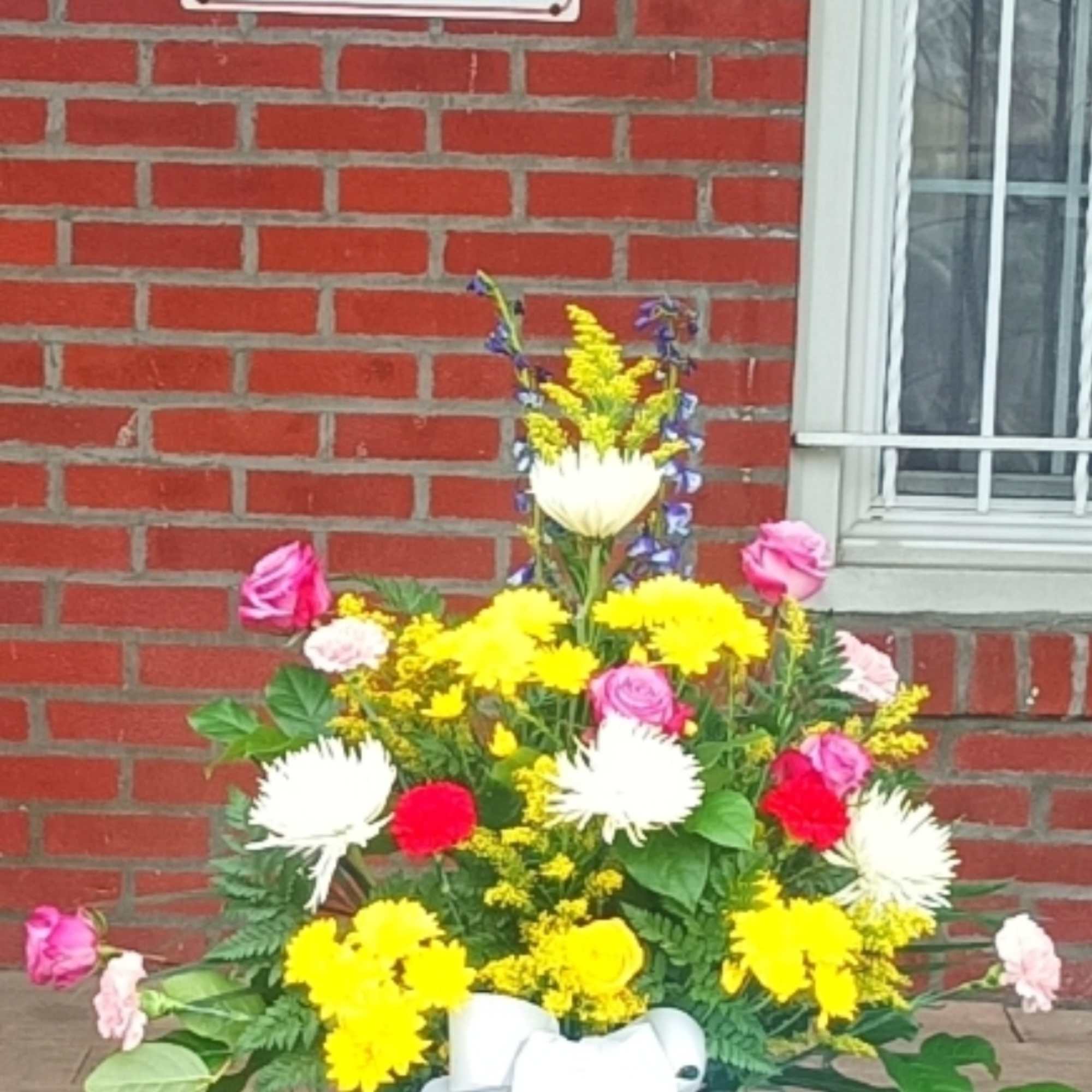 Colorful mixed flower arrangement in a white container with a ribbon