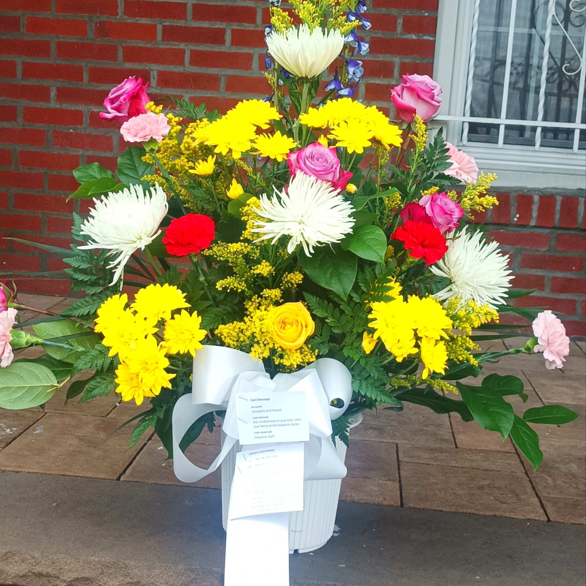 Tall mixed floral arrangement in a white vase with a white ribbon