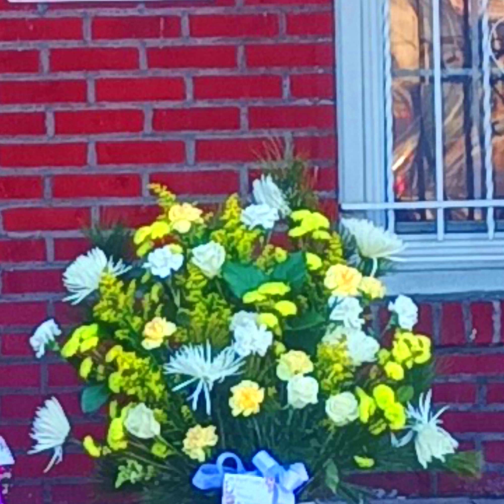Yellow and white floral arrangement in a white vase with a blue ribbon