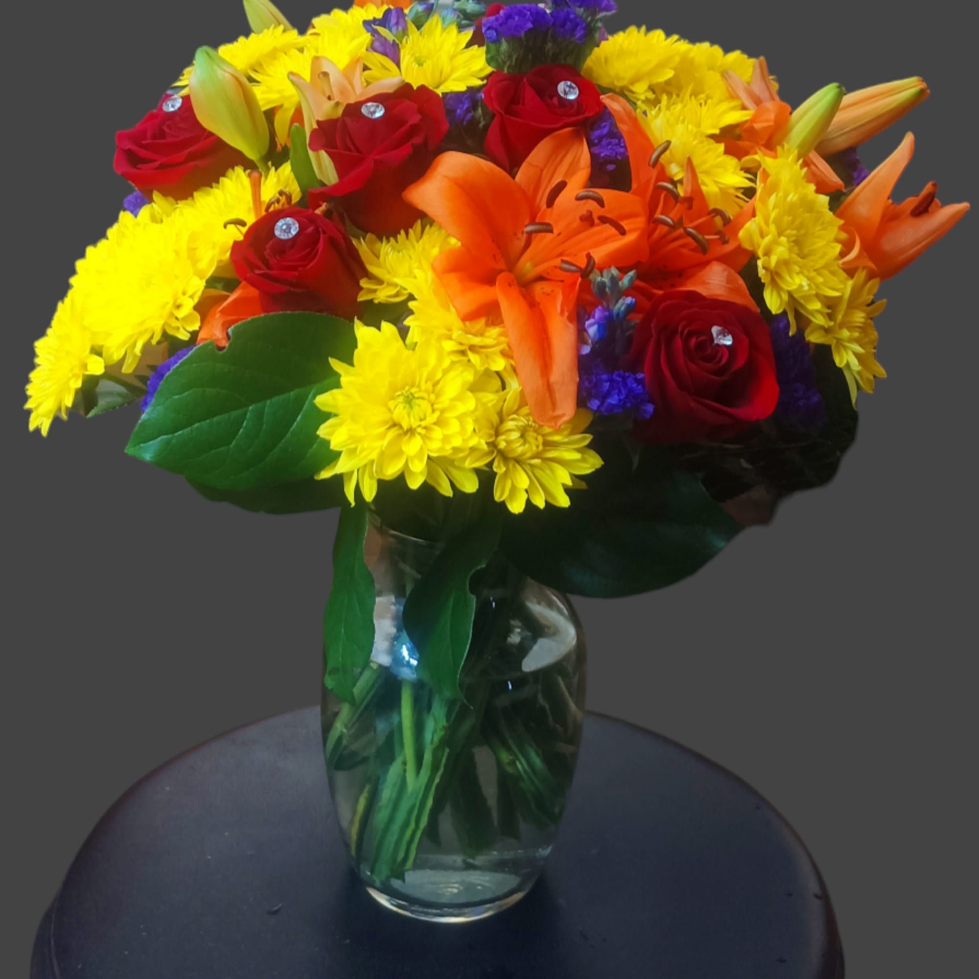 Bouquet of red roses, orange lilies, and yellow mums in a glass vase