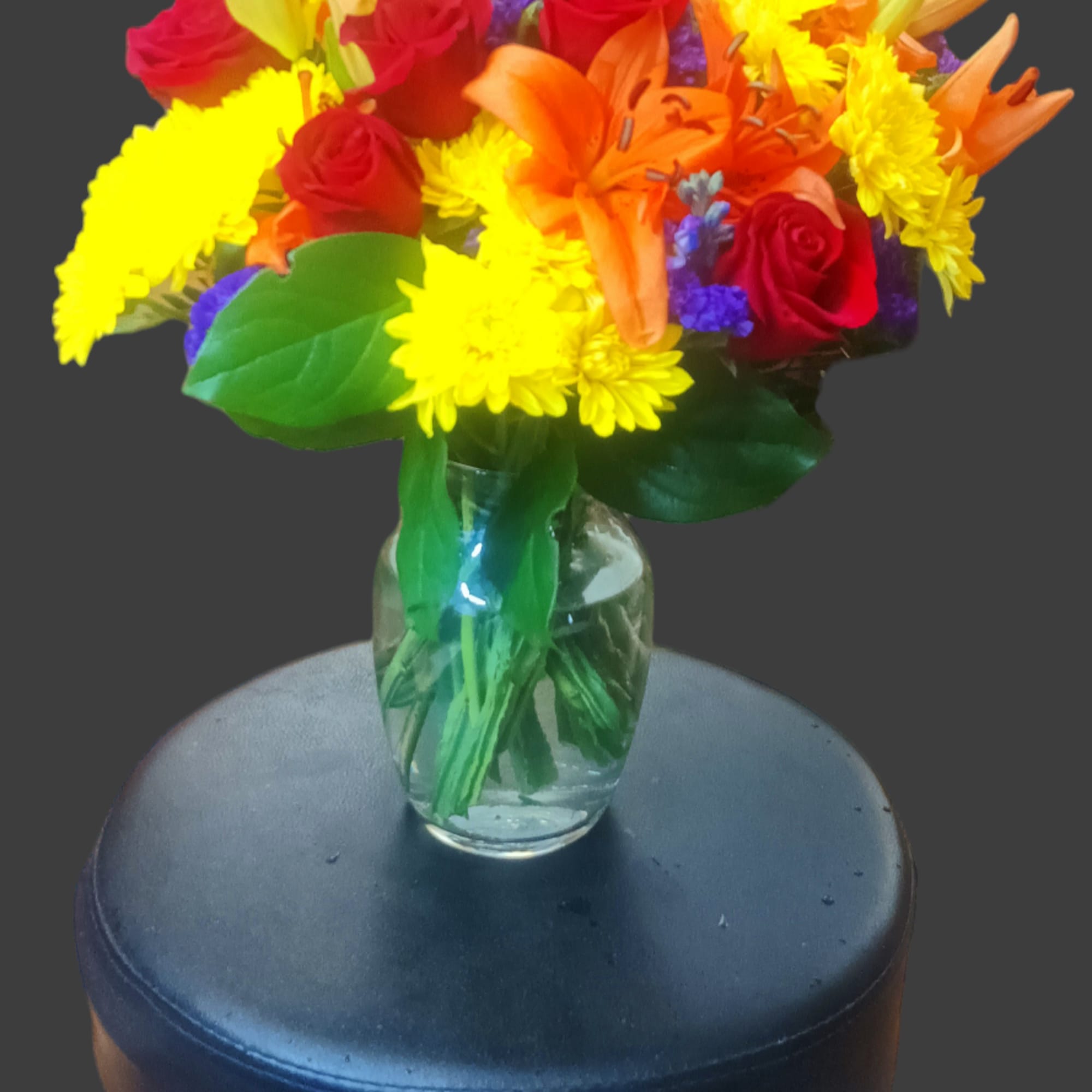 Bouquet of red roses, orange lilies, and yellow daisies in a glass vase