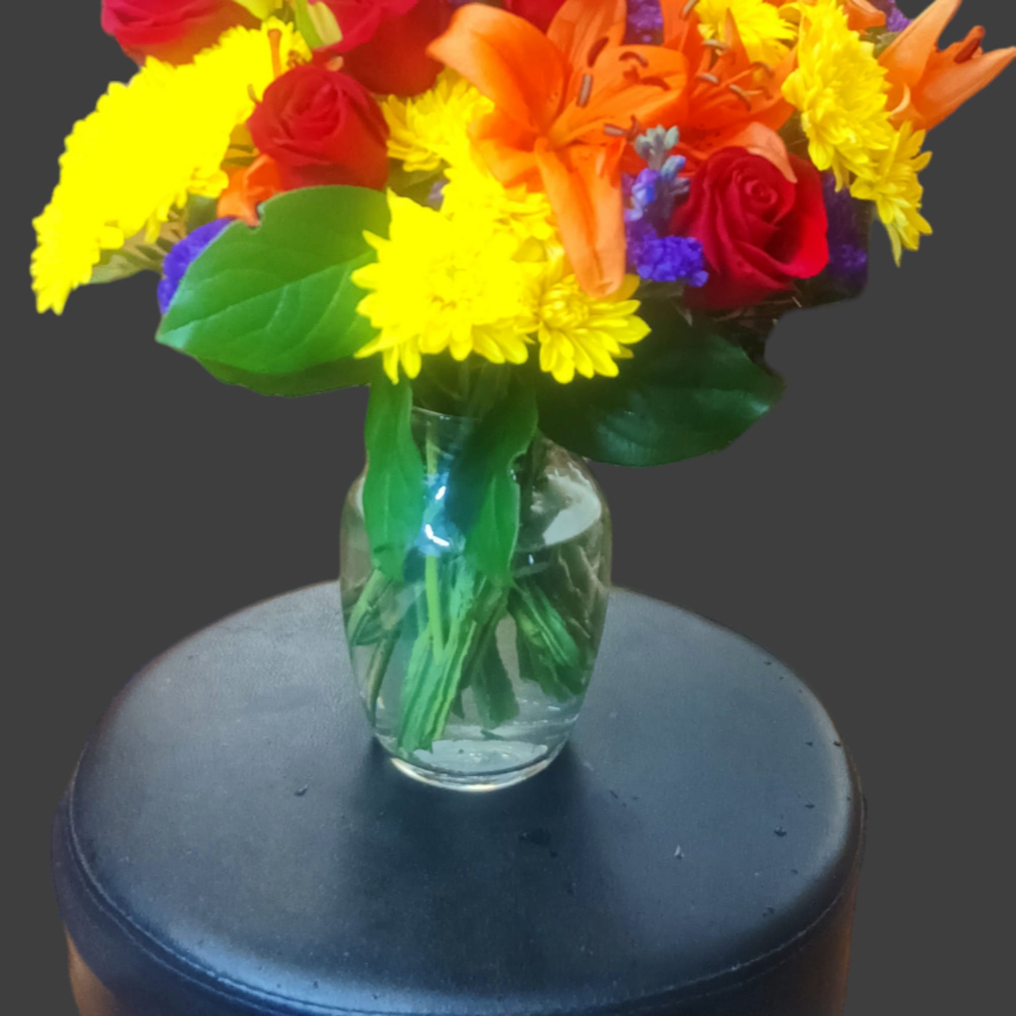 Mixed bouquet of red roses, orange lilies, and yellow daisies in a glass vase