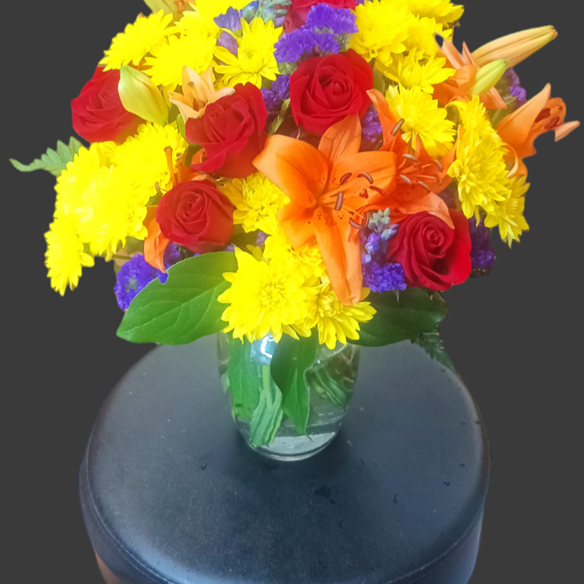Bouquet of red roses, yellow mums, and orange lilies in a glass vase