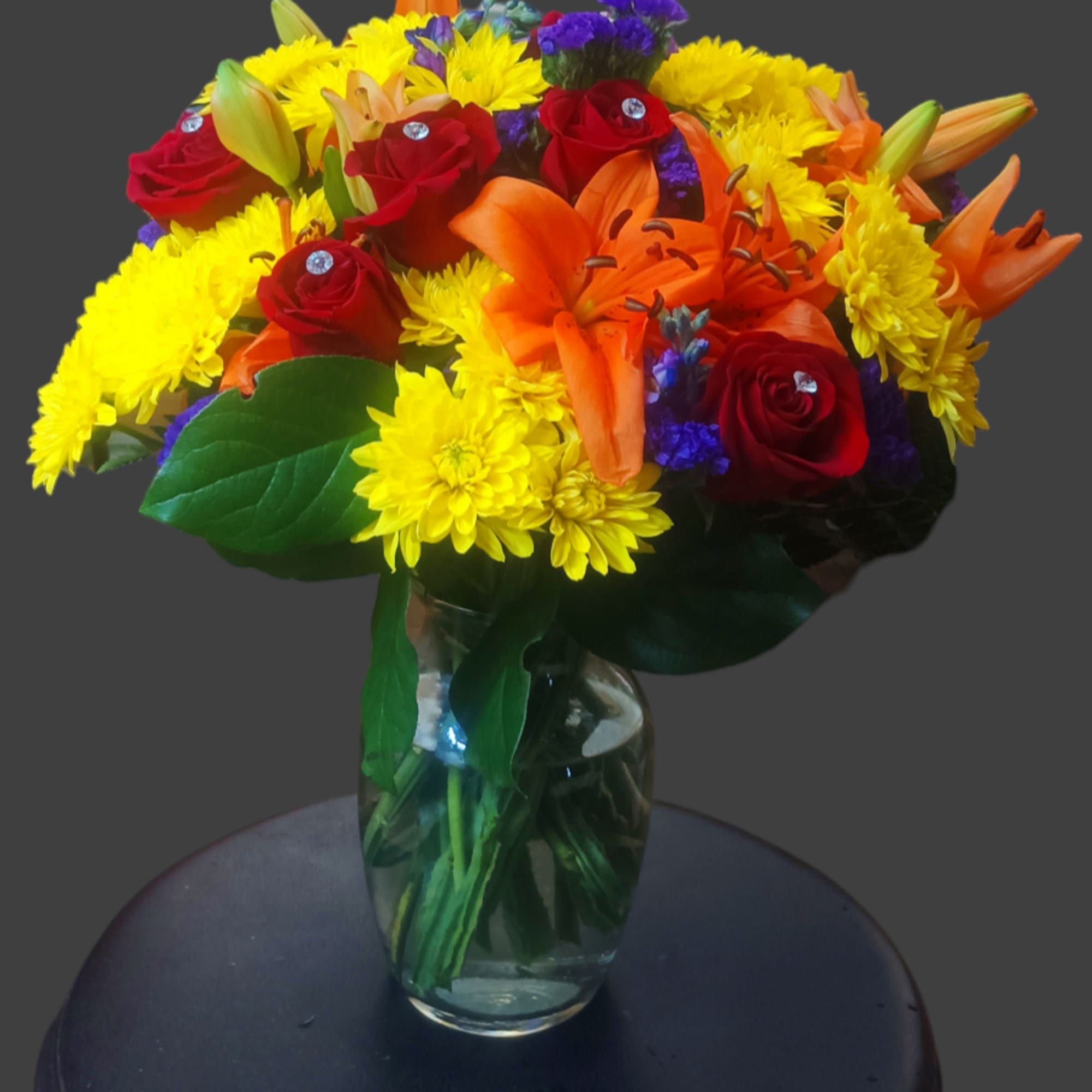 Bouquet of red roses, orange lilies, and yellow chrysanthemums in a glass vase
