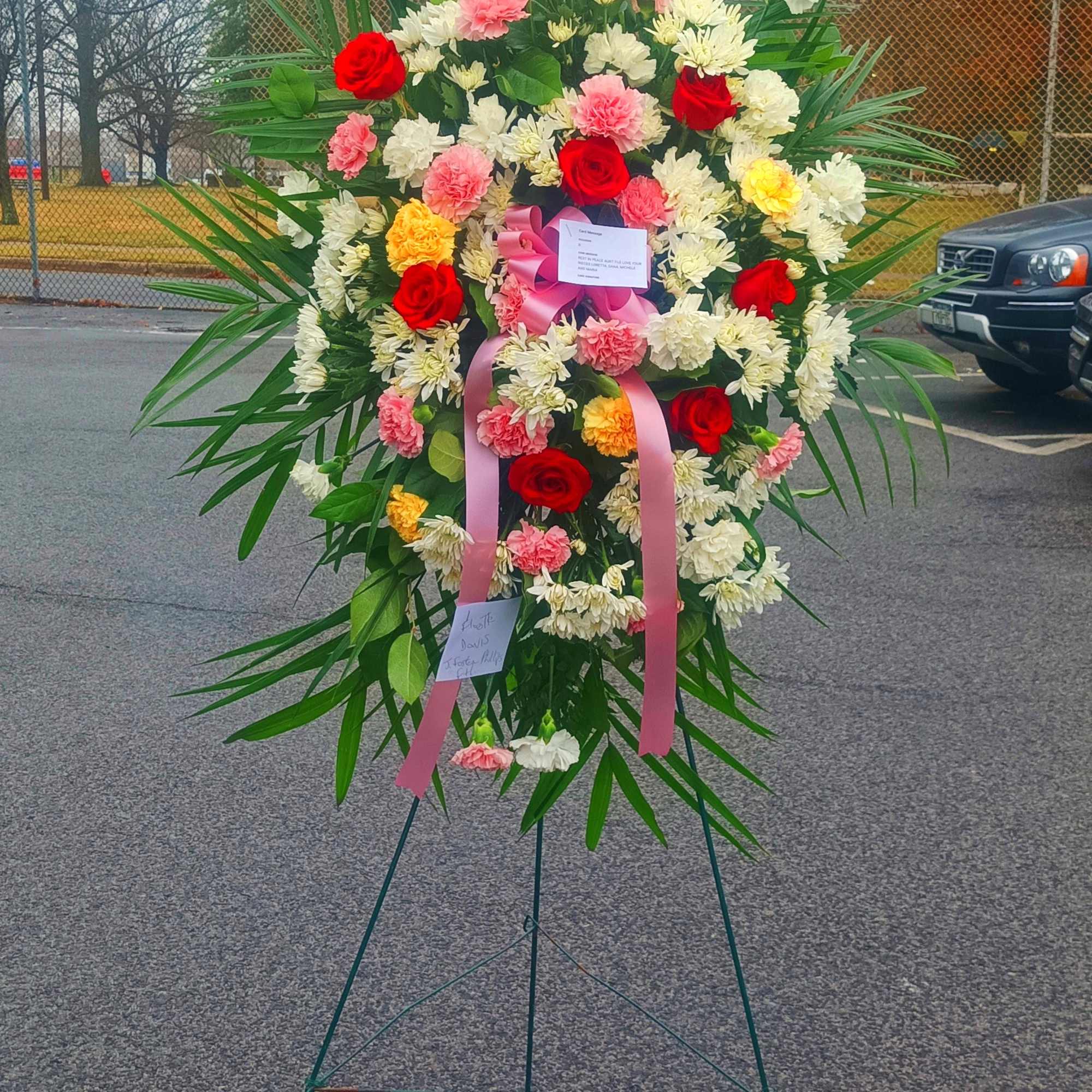 Large standing floral wreath with red, pink, and white flowers on an easel